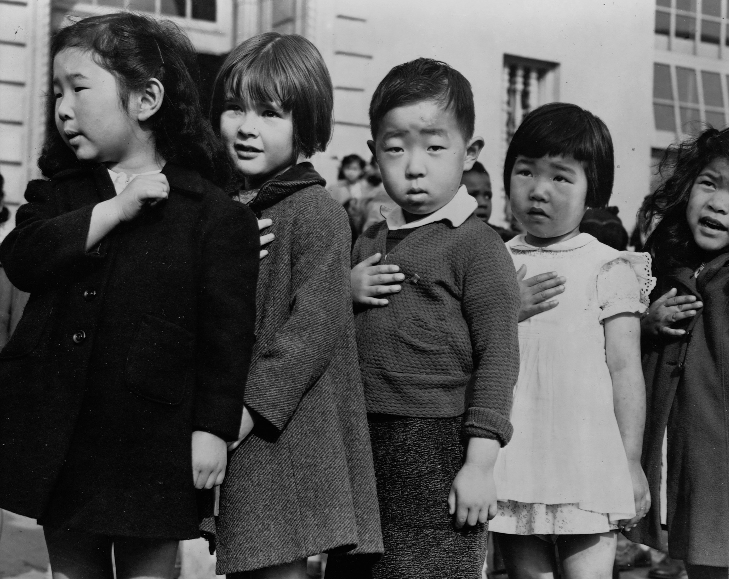 Japanese-American children stand in line, hands over their hearts, saying the Pledge of Allegiance to the American flag at Weill Public School in San Francisco, Calif., before being taken to relocation camps during World War II.