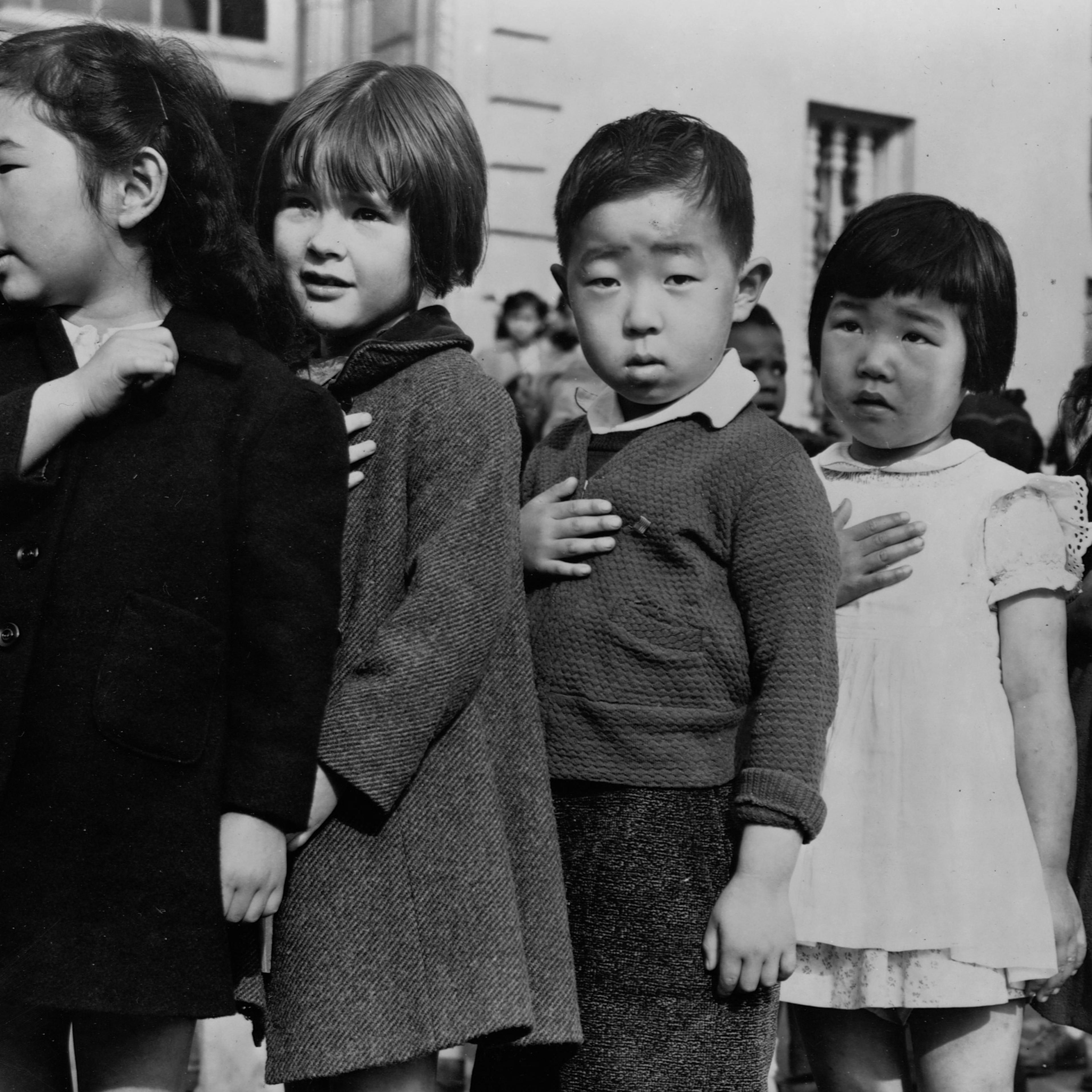 Japanese-American children stand in line, hands over their hearts, saying the Pledge of Allegiance to the American flag at Weill Public School in San Francisco, Calif., before being taken to relocation camps during World War II.