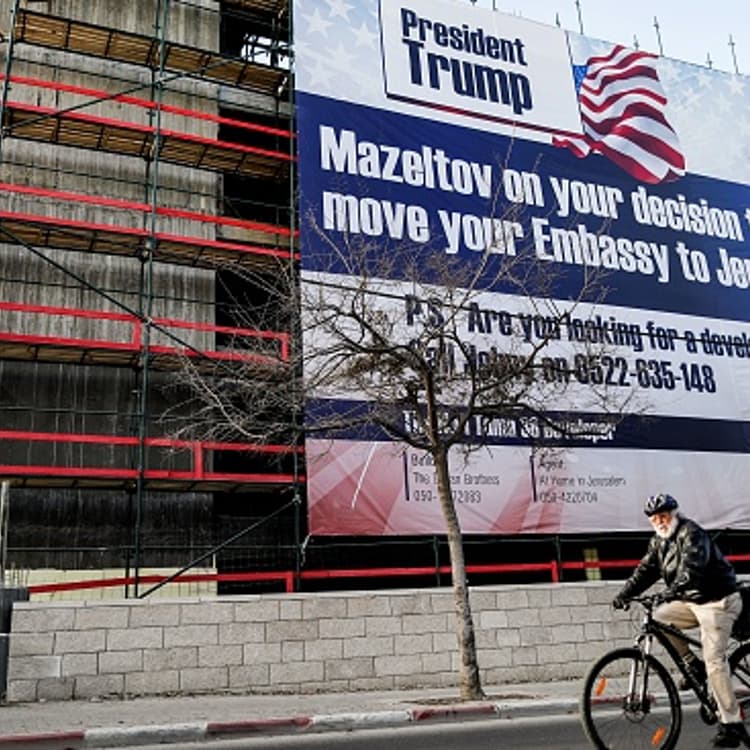A man cycles past a giant banner, bearing a message of congratulations (Mazeltov) for incoming US President Donald Trump, covering a building under construction in central Jerusalem on January 20, 2017.