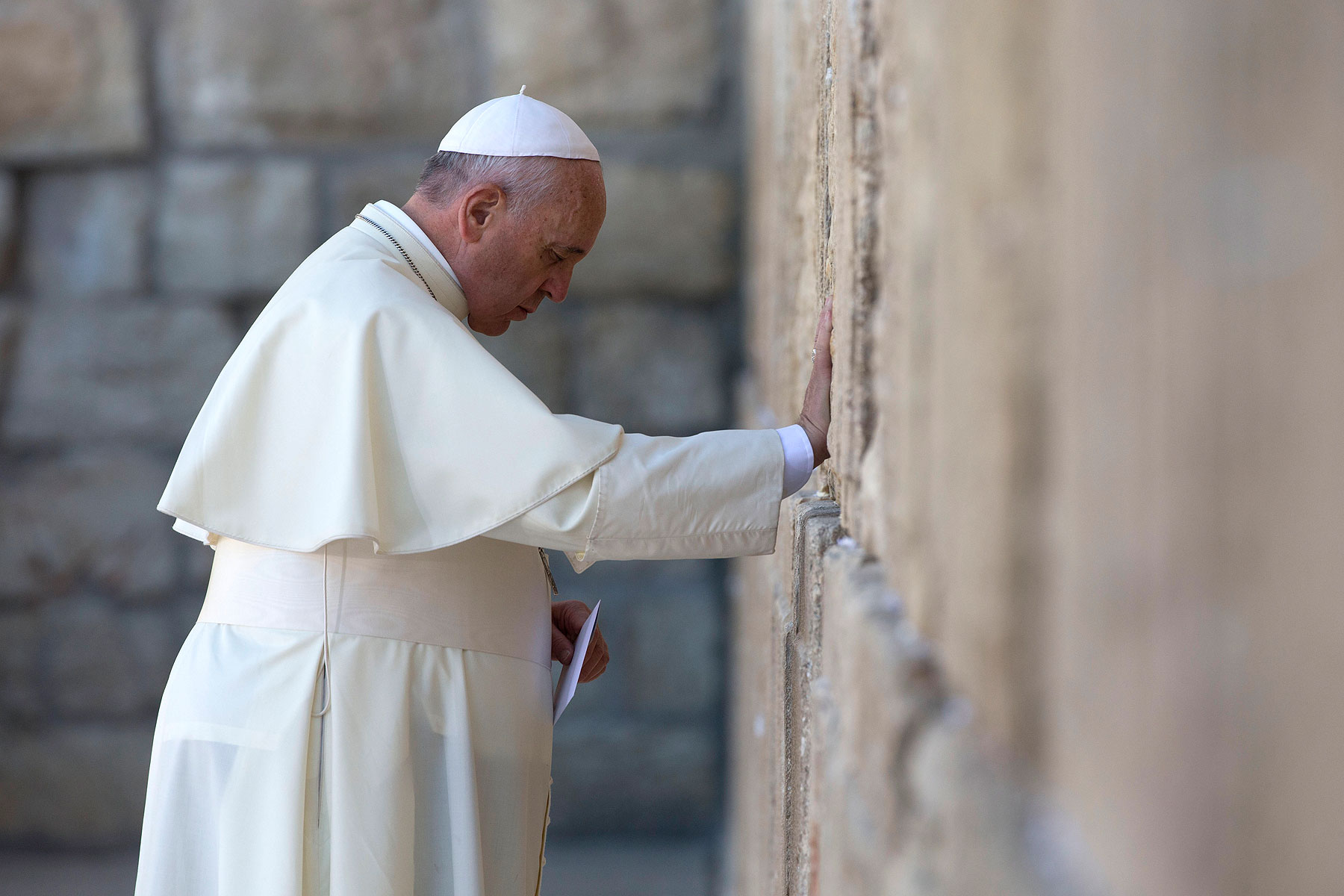 Pope Francis prays as he holds an envelope before placing it in one of the cracks between the stones of the Western Wall, the holiest place where Jews can pray, in Jerusalem on May 26, 2014