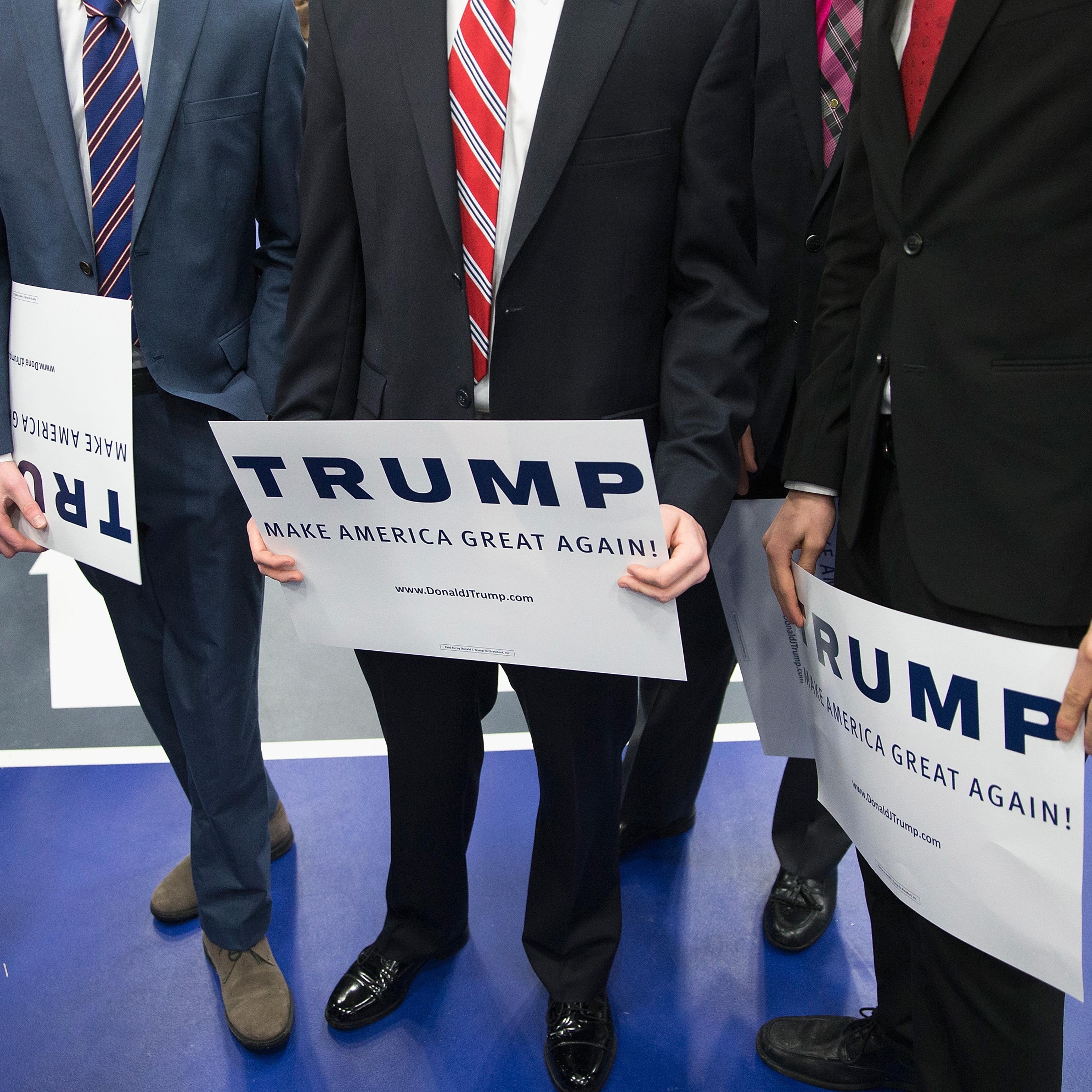 Men hold signs while waiting for Republican presidential candidate Donald Trump to arrive for a rally at Macomb Community College in Warren, Mich., on March 4, 2016.