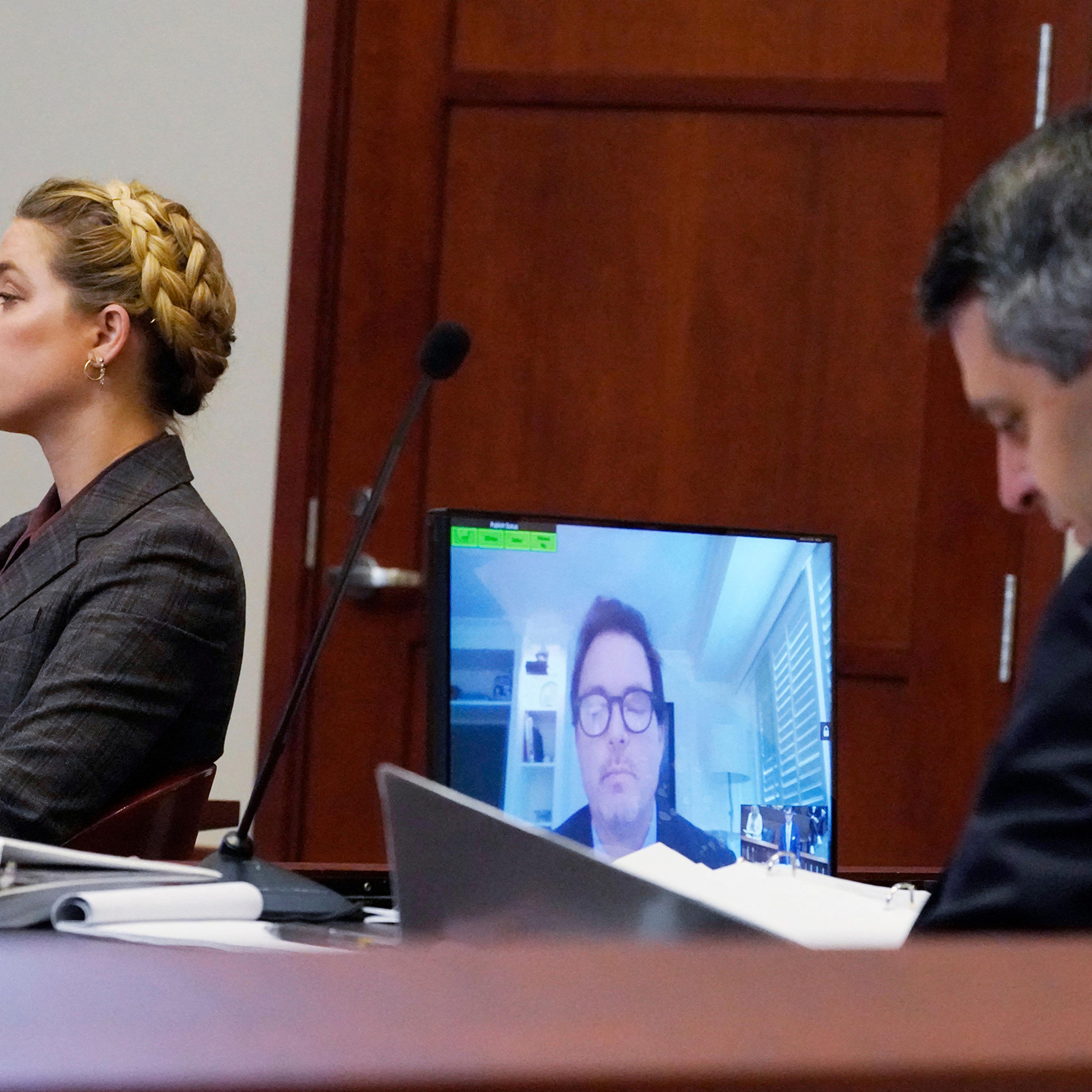 Actress Amber Heard, left, and her attorney, Ben Rottenborn, right, listen as Jack Whigham, center, talent manager for US actor Johnny Depp, is seen on a monitor as he testifies remotely in the courtroom