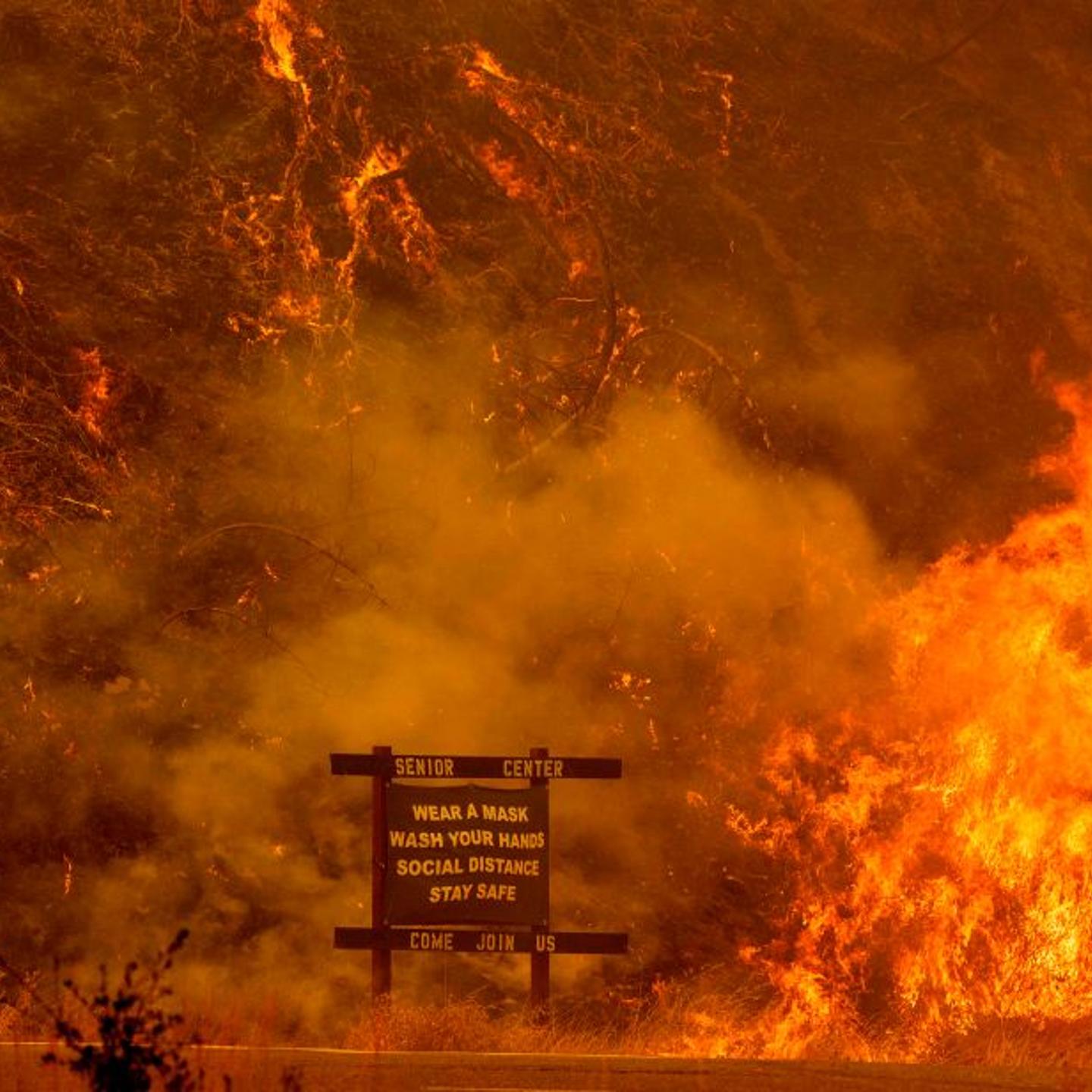 A sign warning people about COVID-19 is surrounded by flames during the Hennessey fire on Aug. 18, 2020, near Lake Berryessa in Napa, Calif.