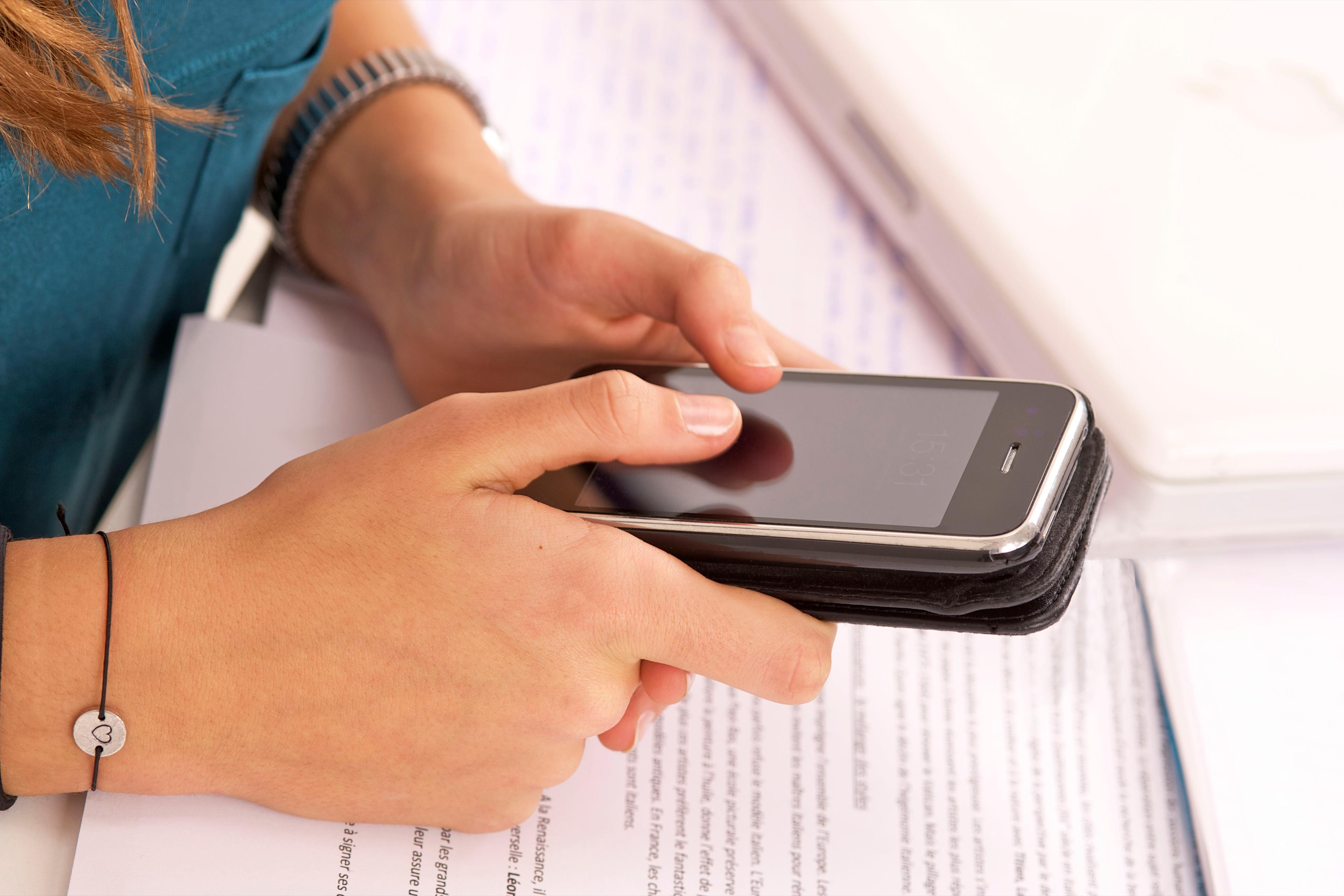 girl using cell phone near textbooks
