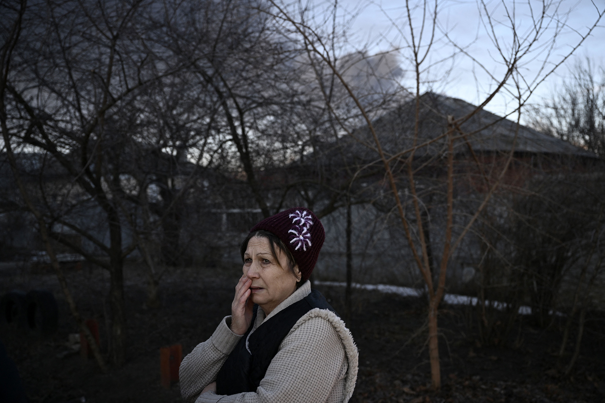 A woman stands in a street as black smoke rises from a military airport in Chuguyev on Feb. 24.