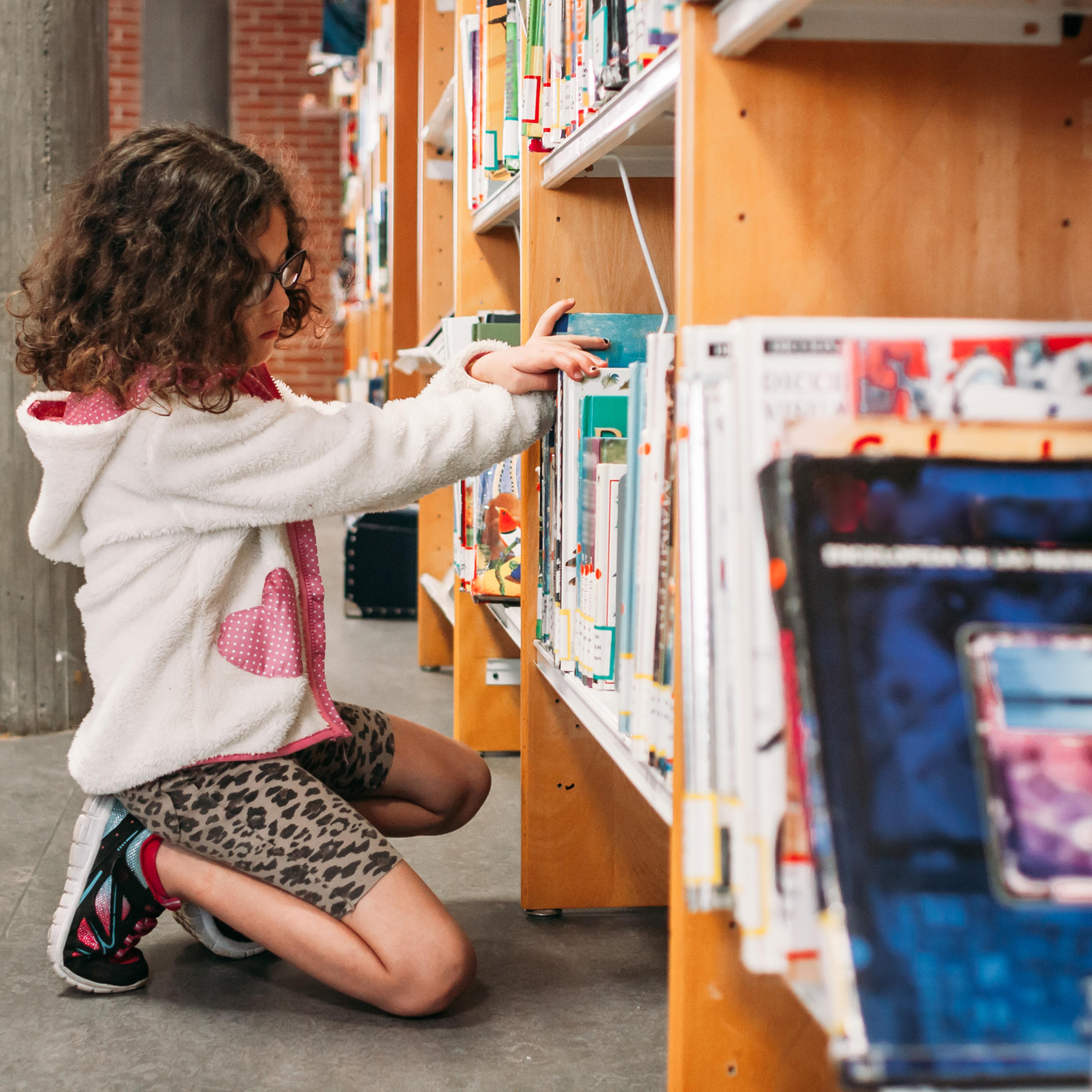 Girl choosing books from the shelves of the public library