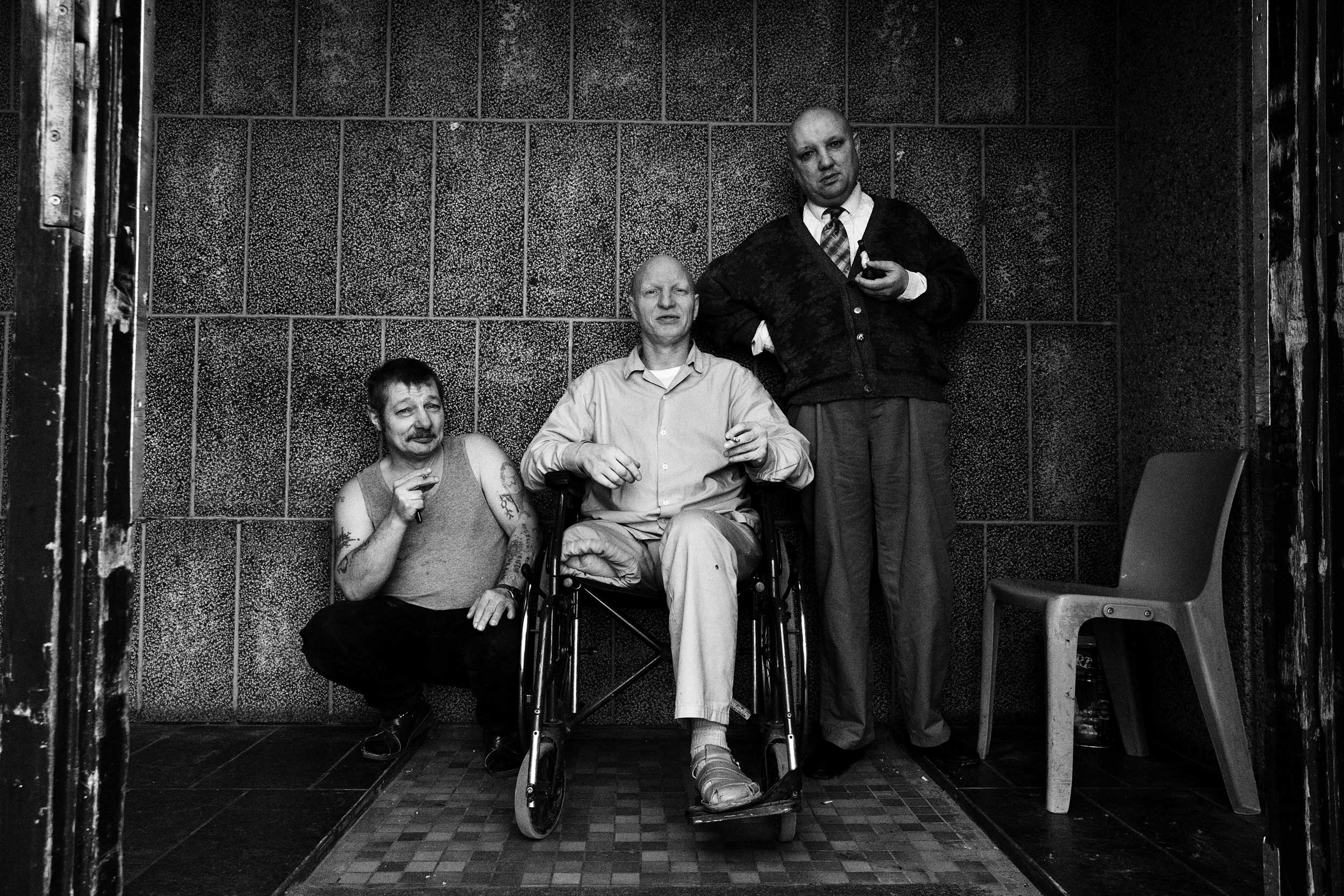 Three mentally-ill prisoners are smoking in front of the entrance to the prison's inner courtyard. Paifve, Liège, Belgium. February 2011.