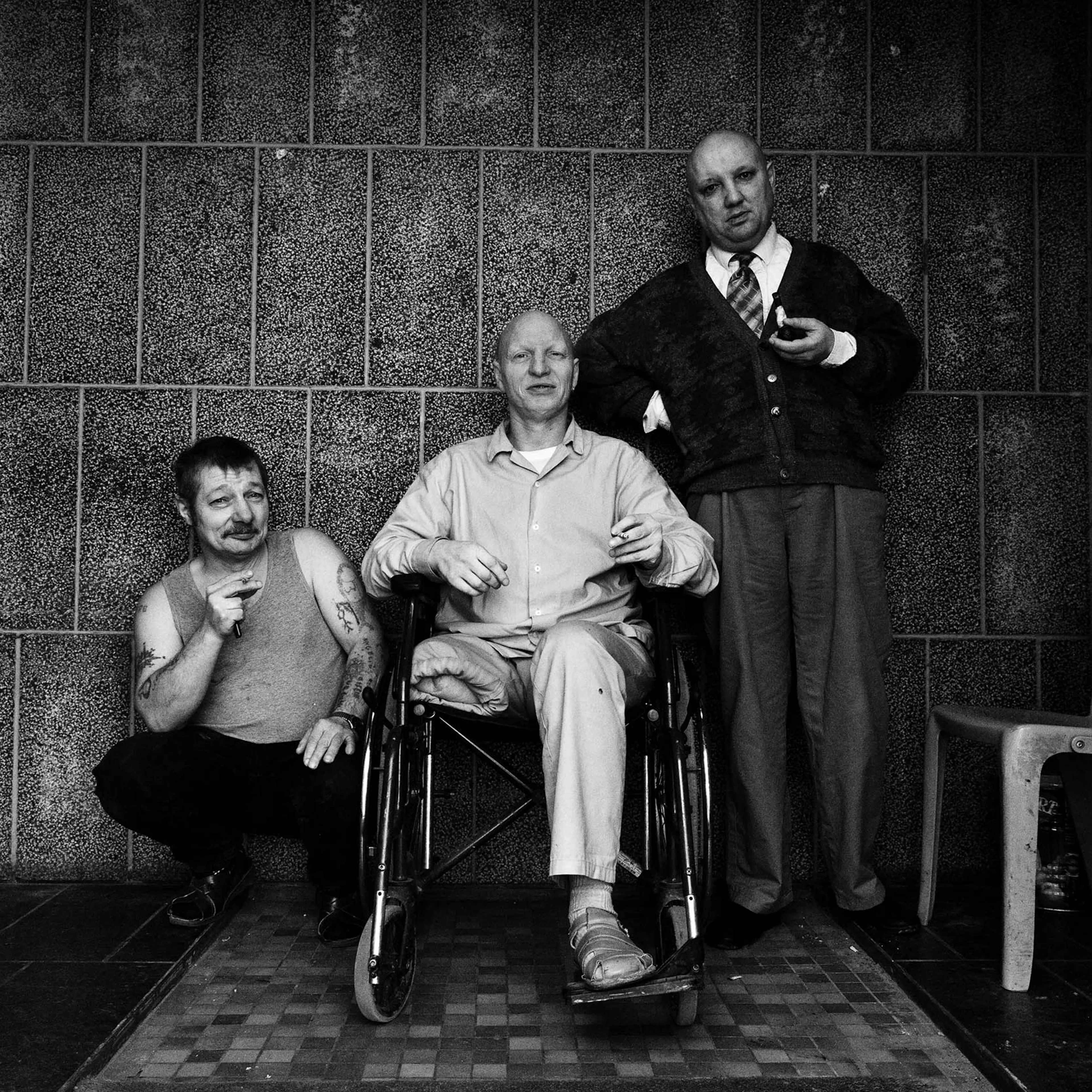 Three mentally-ill prisoners are smoking in front of the entrance to the prison's inner courtyard. Paifve, Liège, Belgium. February 2011.