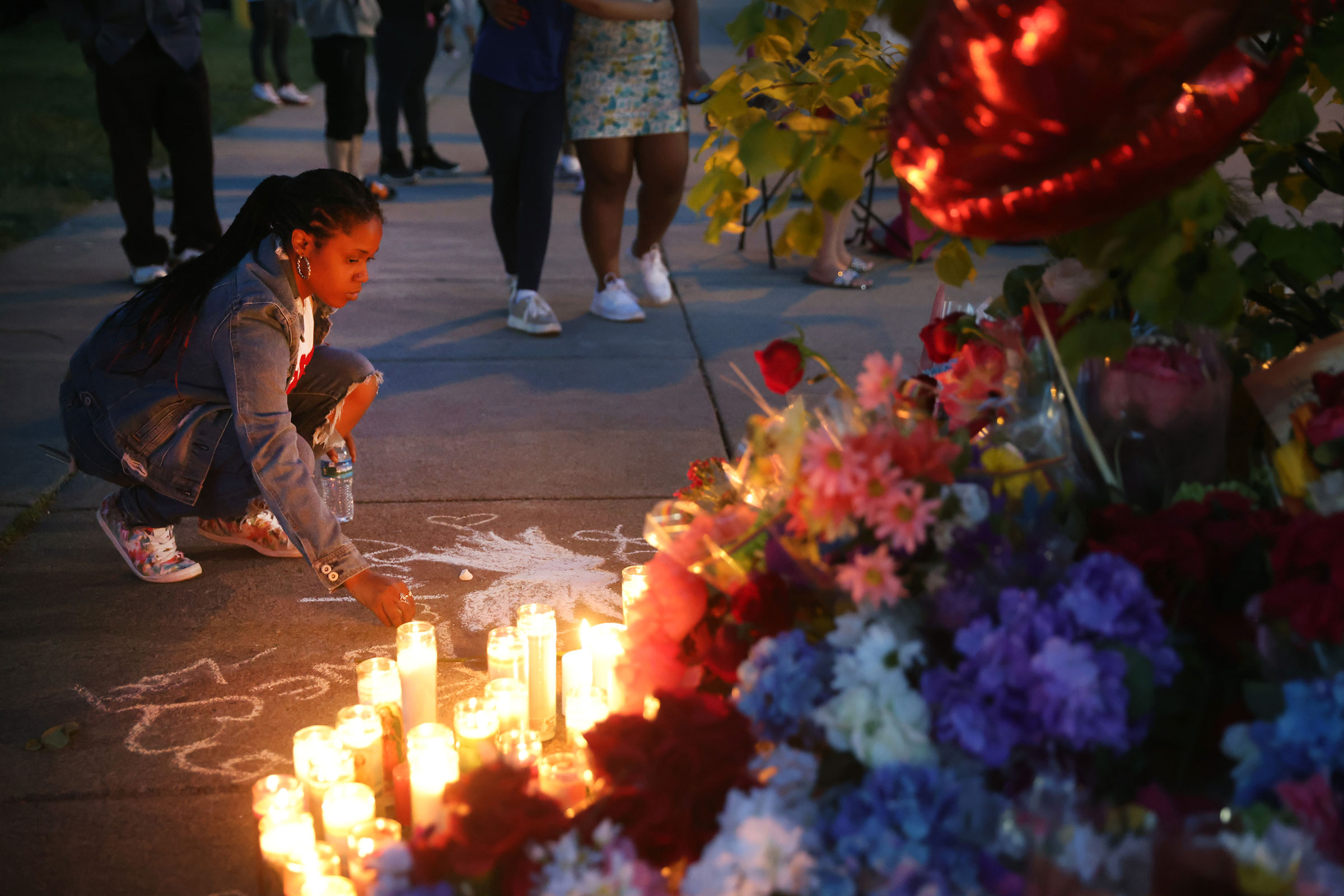 A woman chalks a message at a makeshift memorial outside of Tops market