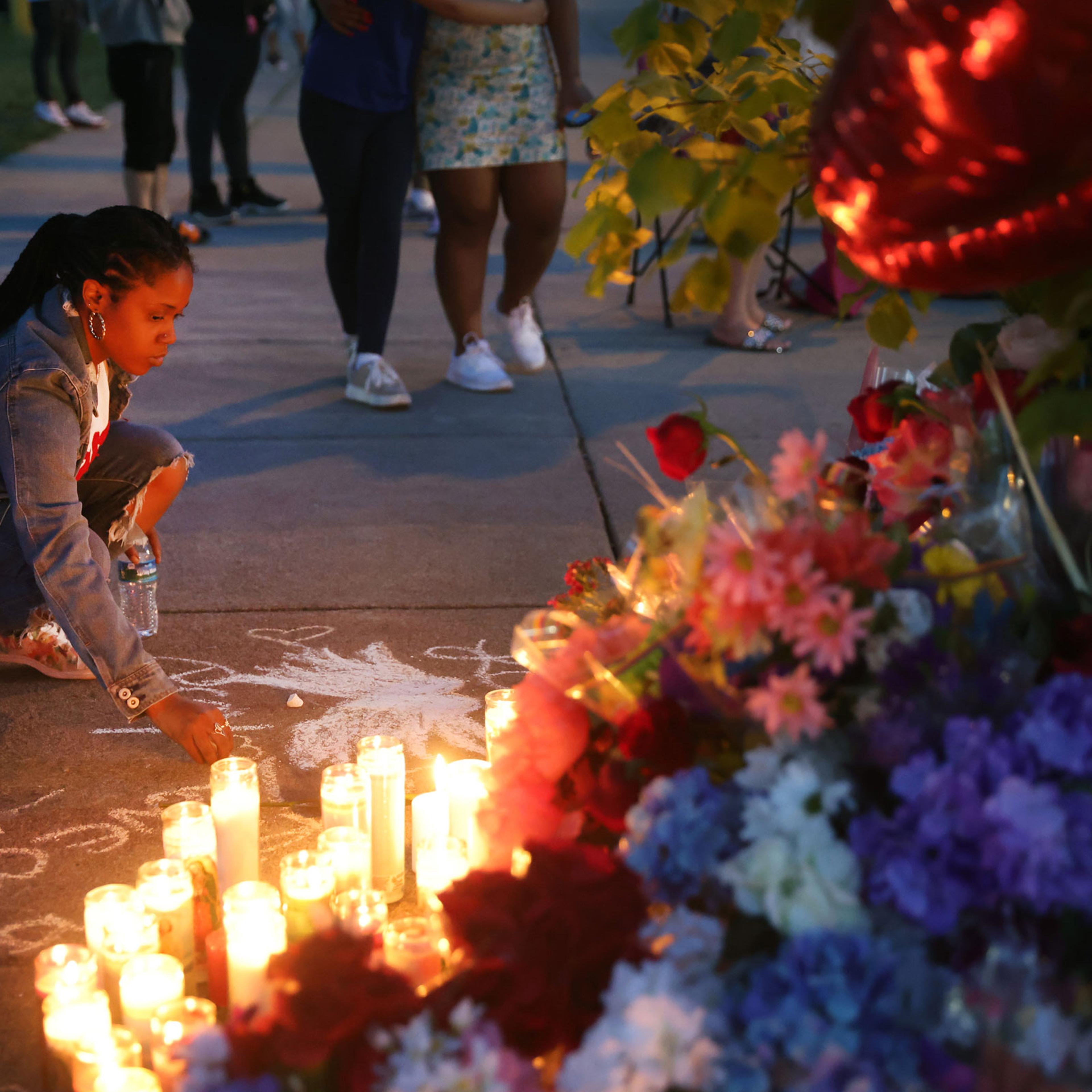 A woman chalks a message at a makeshift memorial outside of Tops market