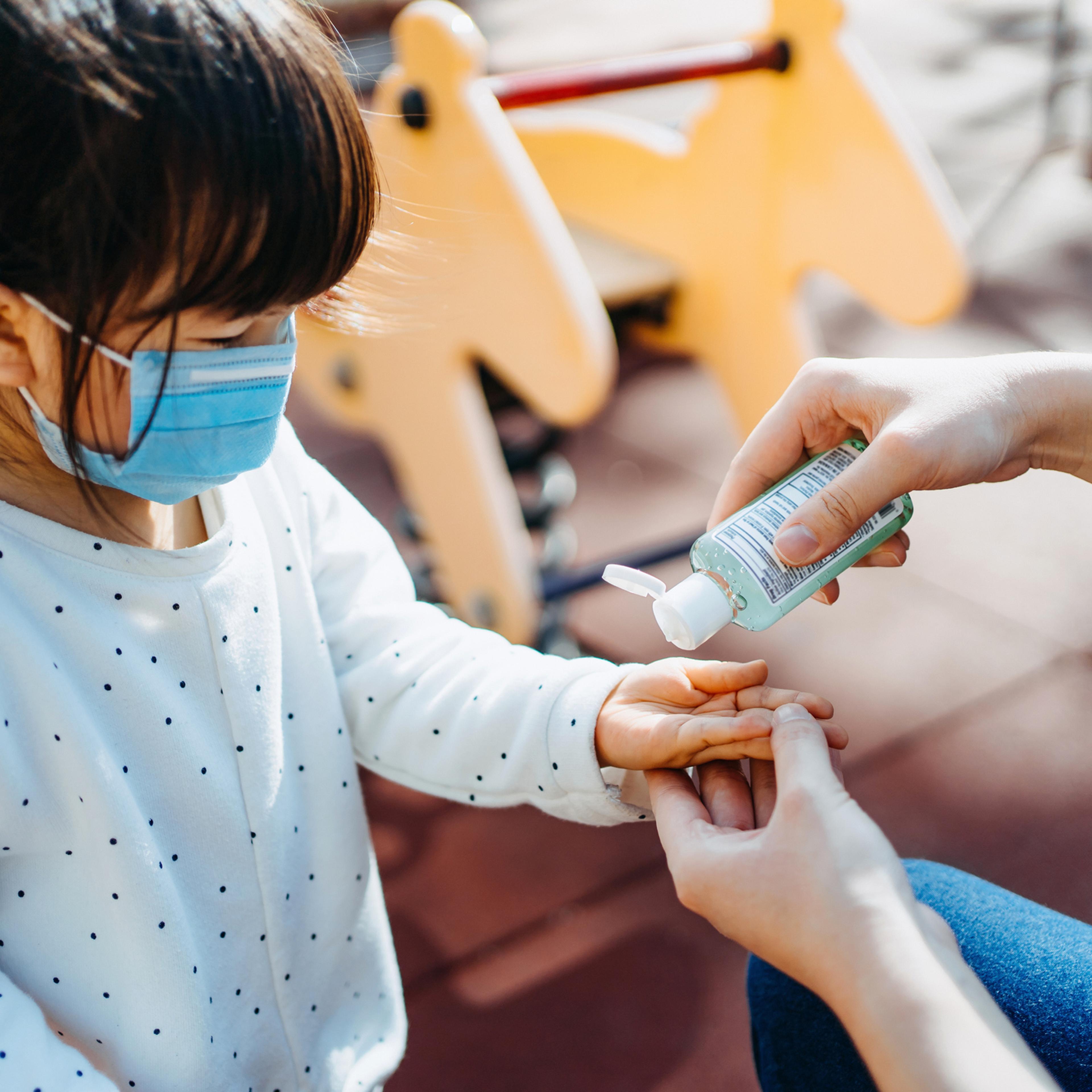 Young mother squeezing hand sanitizer onto little daughter's hand in the playground to prevent the spread of viruses
