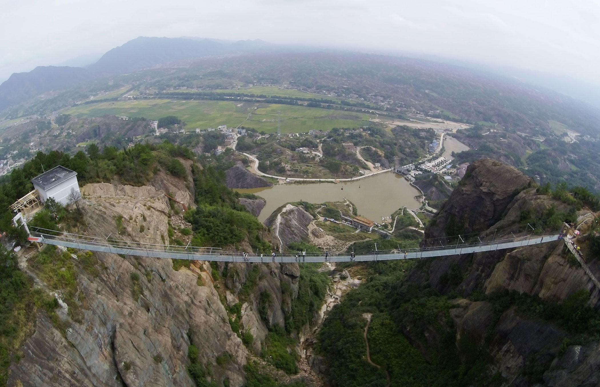 PINGJIANG, CHINA - SEPTEMBER 24: (CHINA OUT) Tourists walk on a suspension bridge made of glass at the Shiniuzhai National Geological Park on September 24, 2015 in Pingjiang County, China. The 300-meter-long glass suspension bridge, with a maximum height