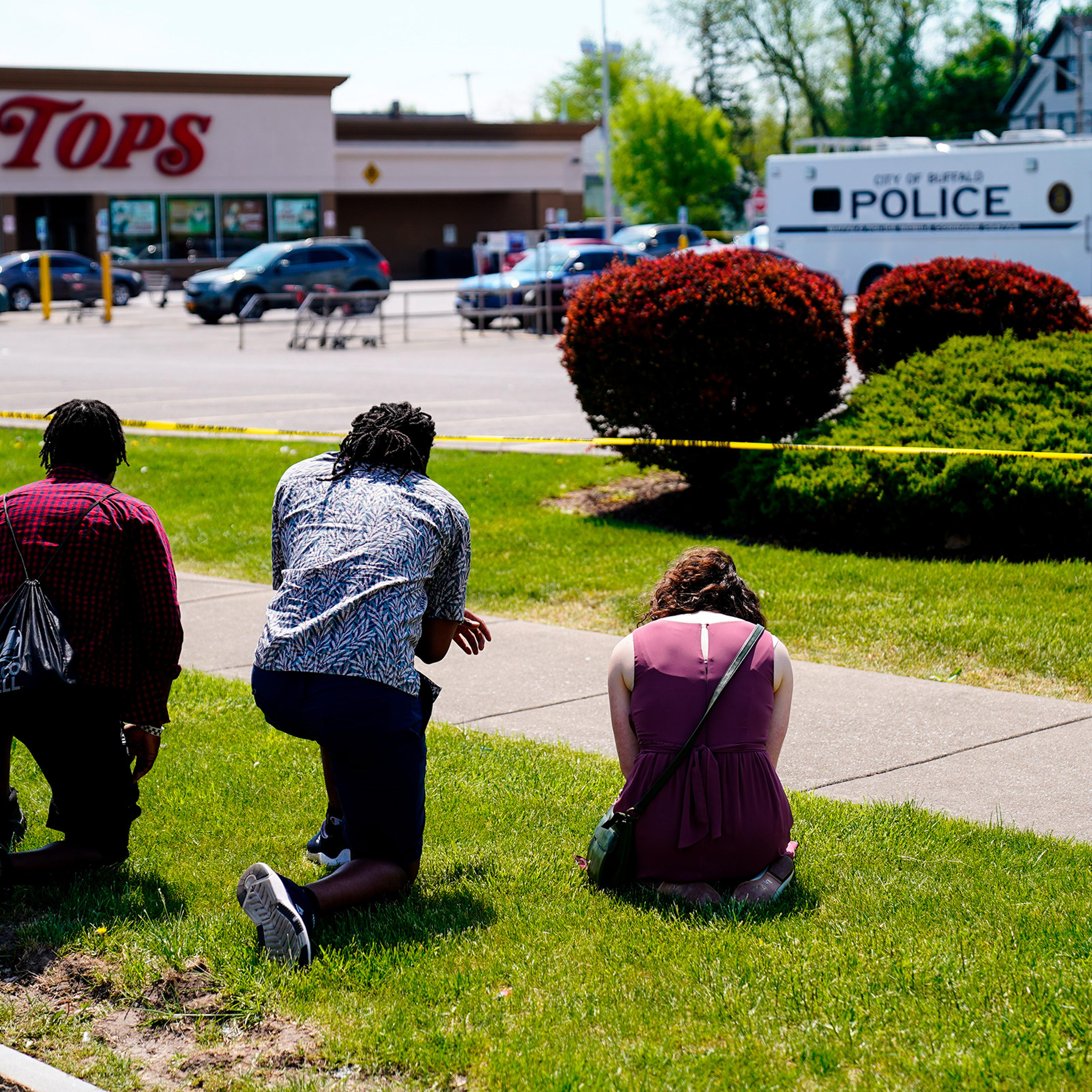 People pray outside the scene of a shooting at Tops supermarket in Buffalo, N.Y., May 15, 2022.