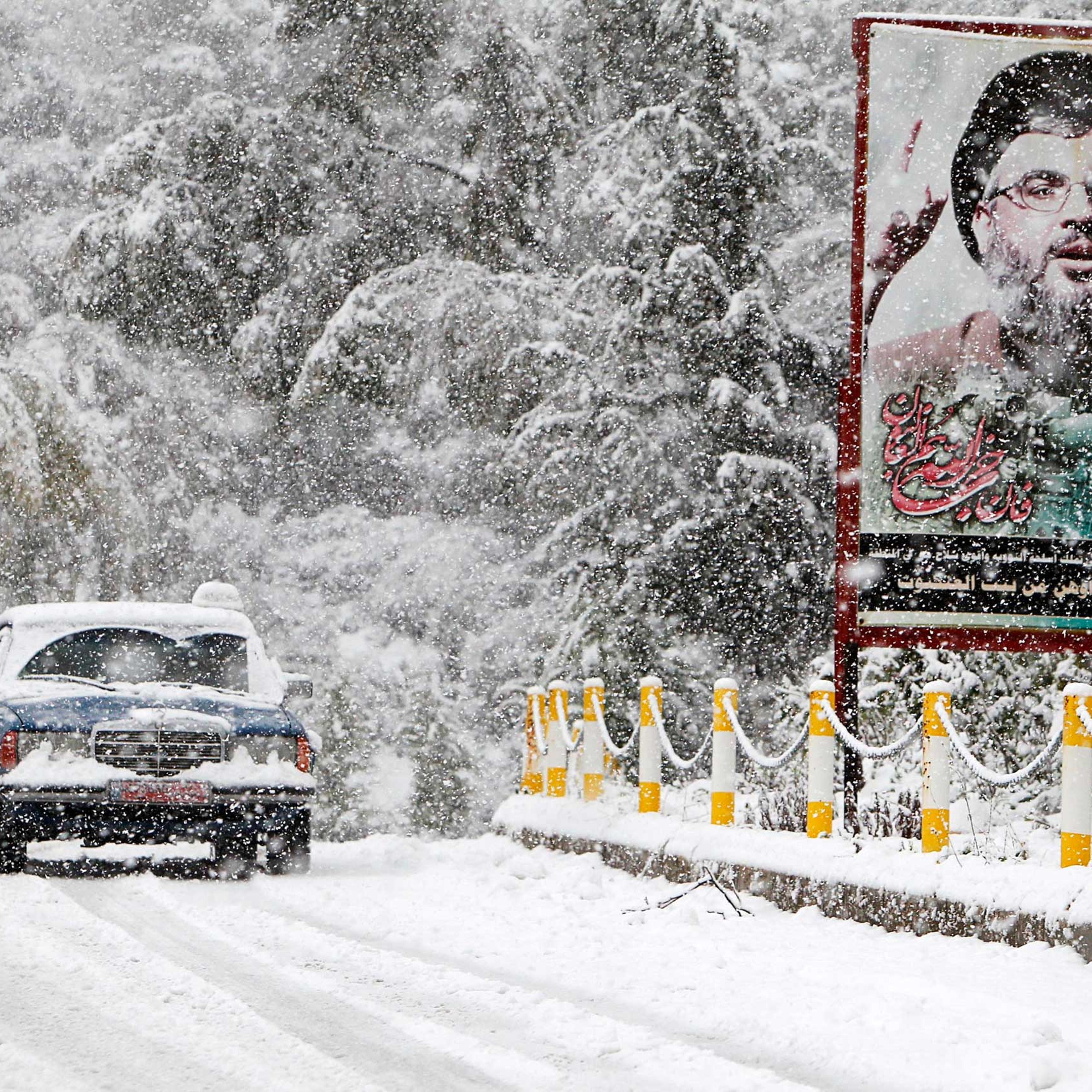 A snow covered taxi drives past a picture of Lebanon's Hezbollah leader Sayyed Hasan Nasrallah in Jbaa village, south Lebanon, Feb. 20, 2015.