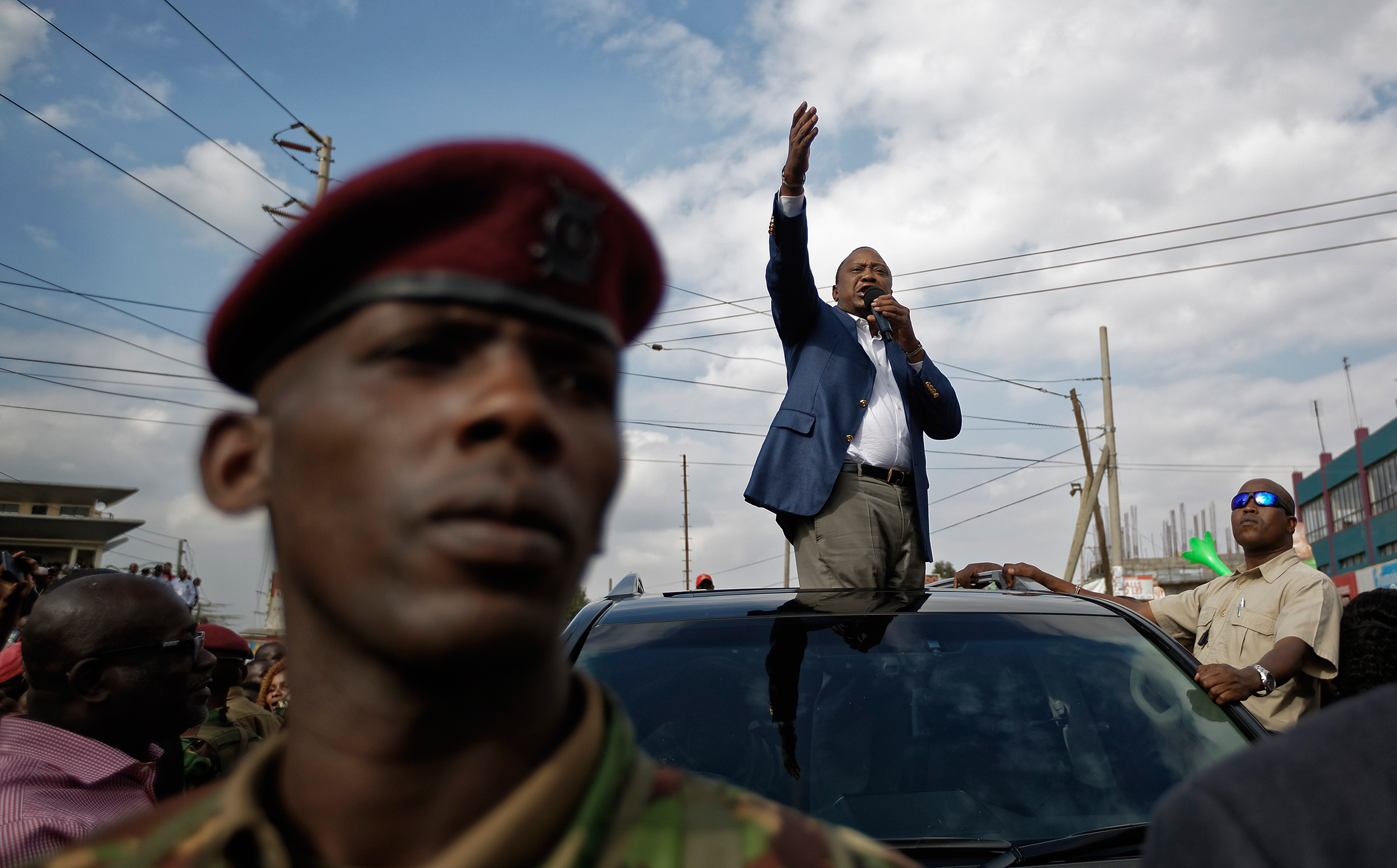 Kenya's President Uhuru Kenyatta, standing through the sunroof of the presidential vehicle, addresses his supporters as a presidential guard provides security, left, on a street in Ongata Rongai, on the outskirts of Nairobi, Kenya, Sept. 5, 2017. Kenya f