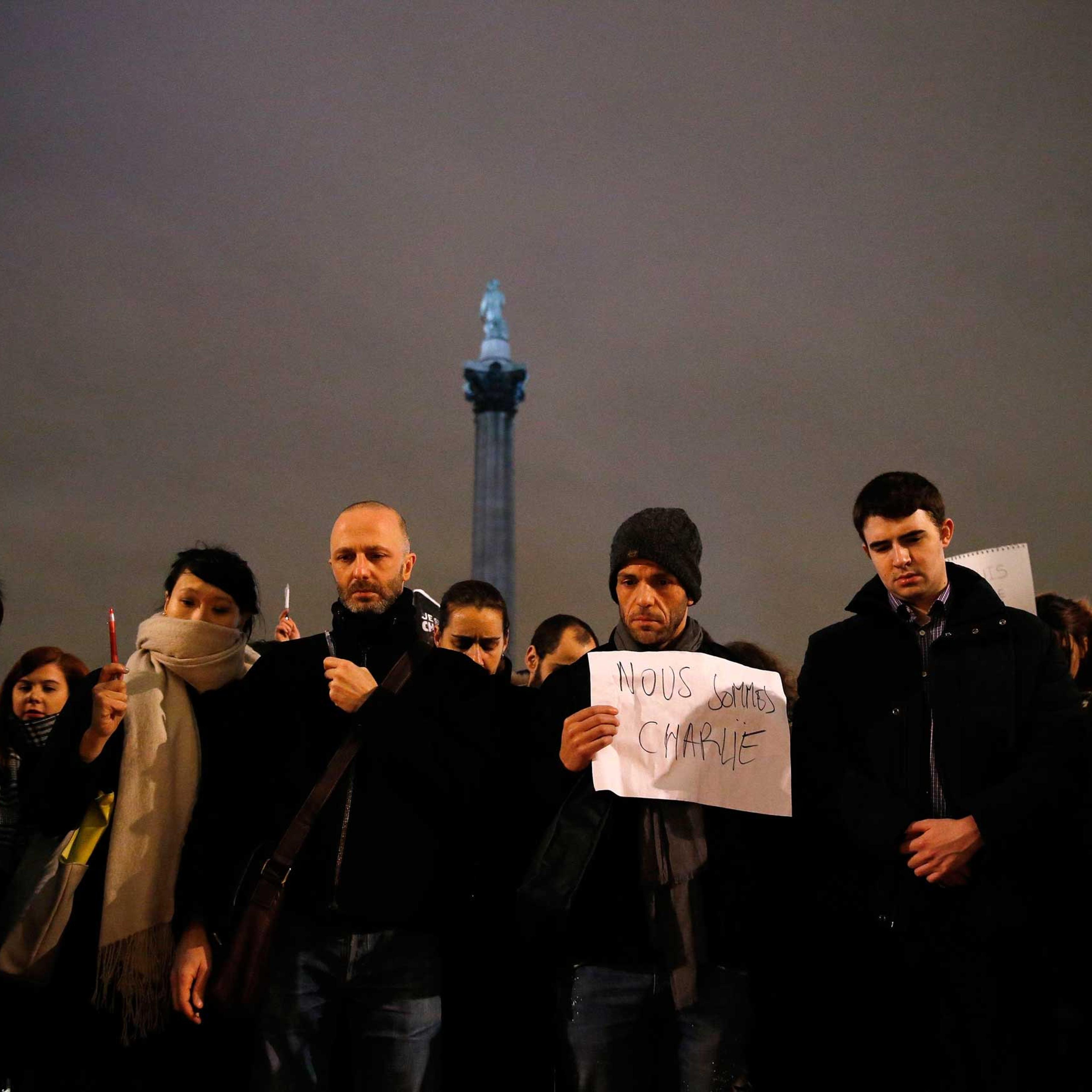 People raise pens and signs during a vigil to pay tribute to the victims of a shooting by gunmen at the offices of weekly satirical magazine Charlie Hebdo in Paris, at Trafalgar Square in London, Jan. 7, 2015.