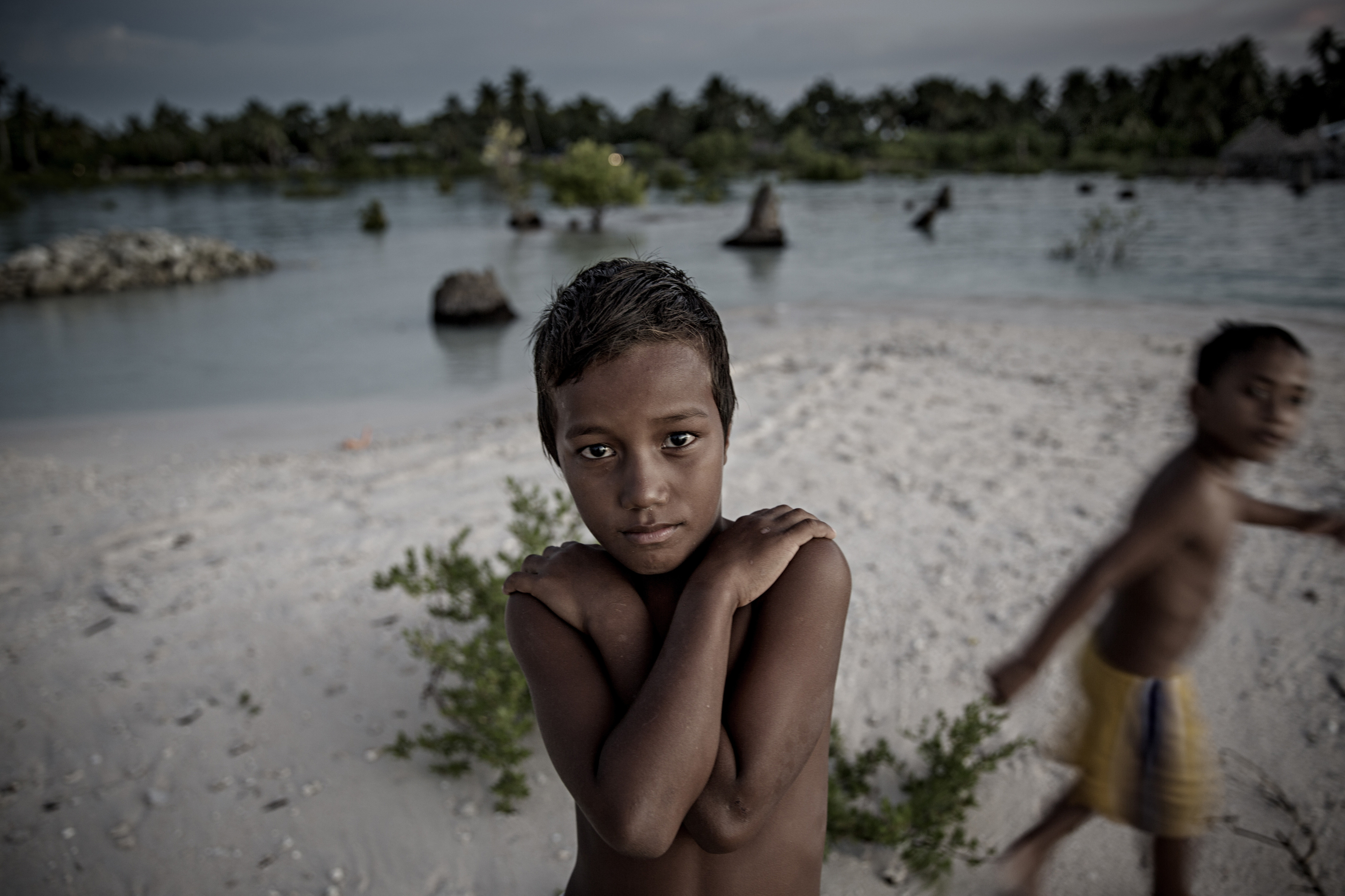 EITA, TARAWA, KIRIBATI - 2015/09/30: A young boy stands on a narrow strip of land that luckily didn't flood and prevented his home from being drowned in the sea with the village Eita. The people of Kiribati are under pressure to relocate due to sea level