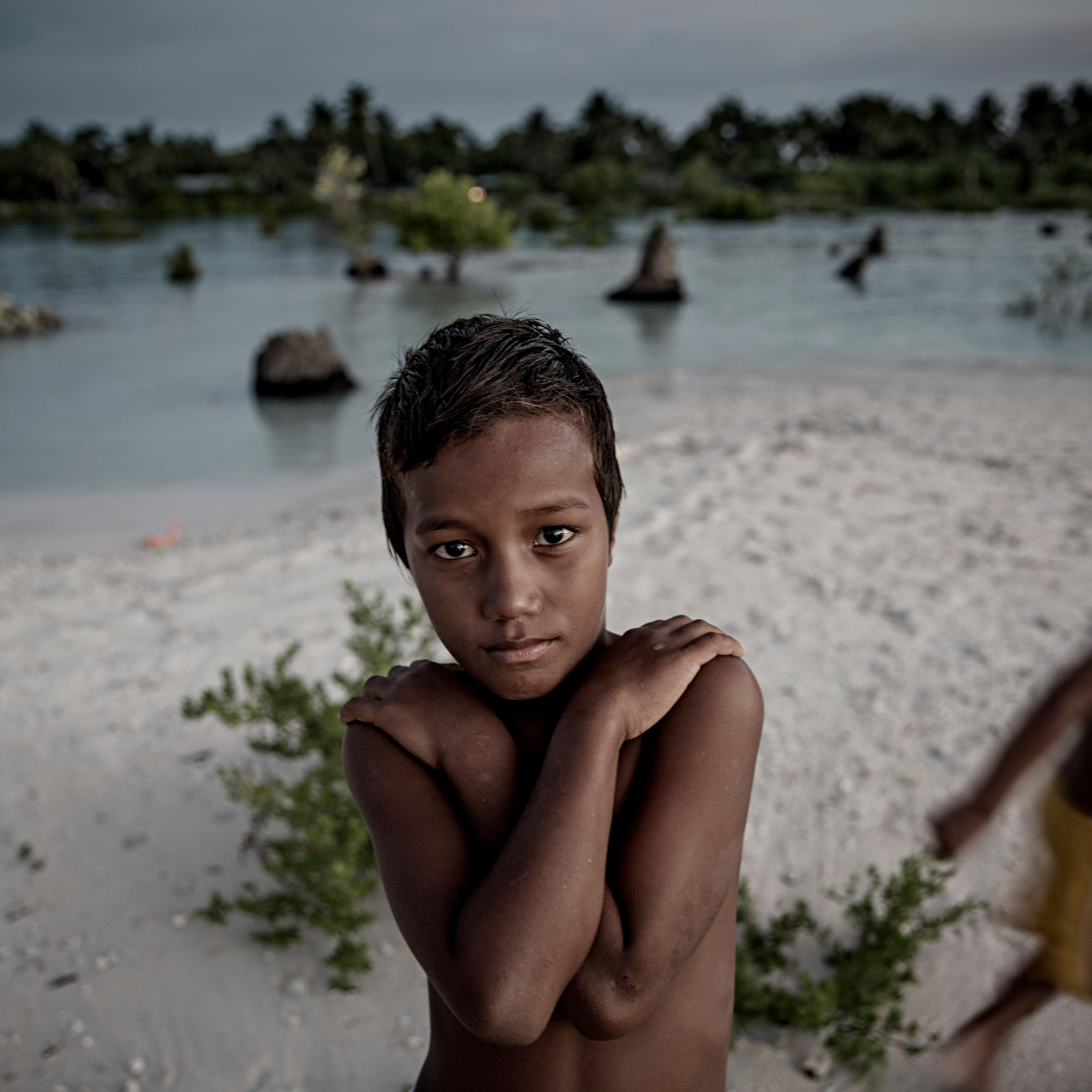 EITA, TARAWA, KIRIBATI - 2015/09/30: A young boy stands on a narrow strip of land that luckily didn't flood and prevented his home from being drowned in the sea with the village Eita. The people of Kiribati are under pressure to relocate due to sea level