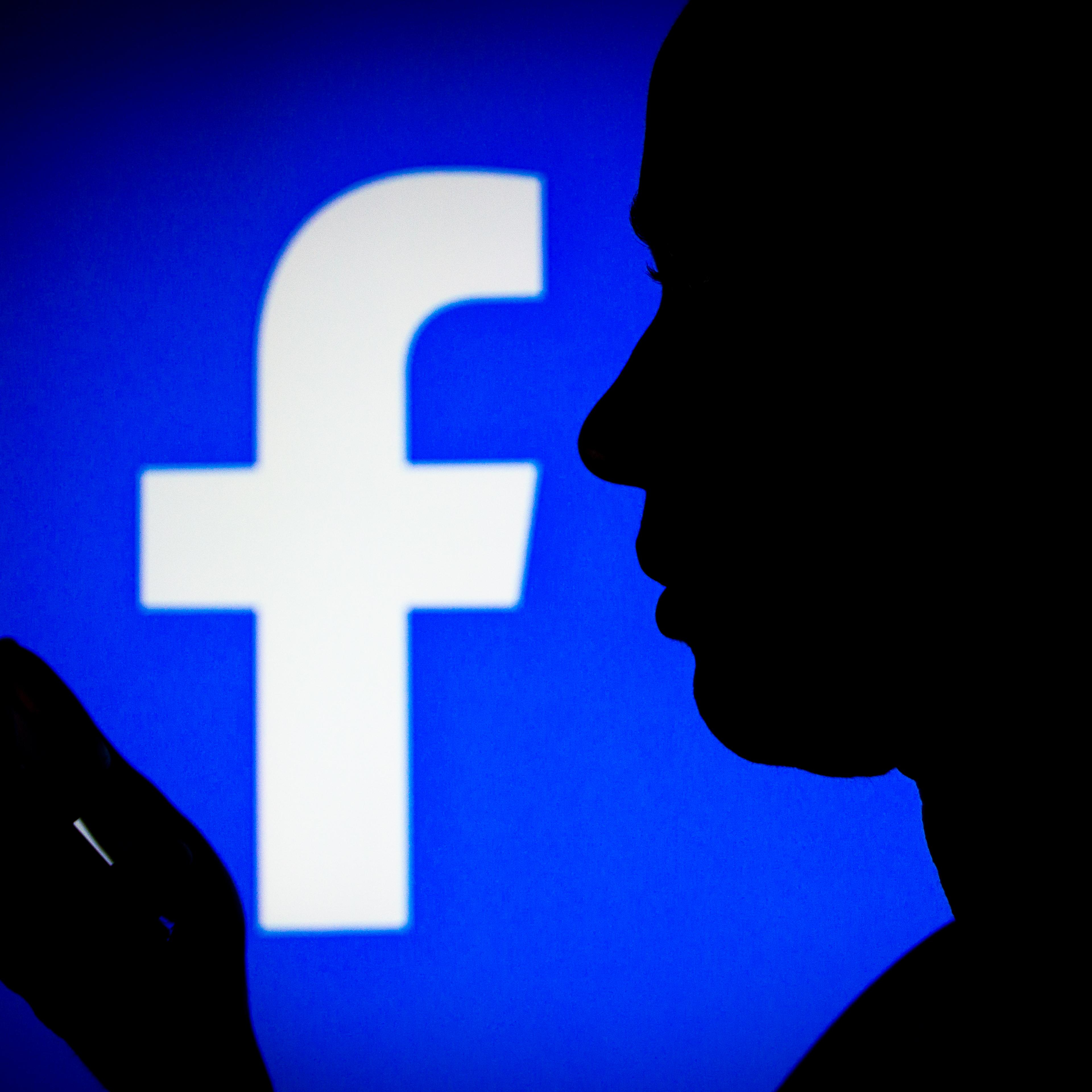 In this photo illustration, the Facebook logo is seen in the background of a silhouette of a woman holding a mobile phone.