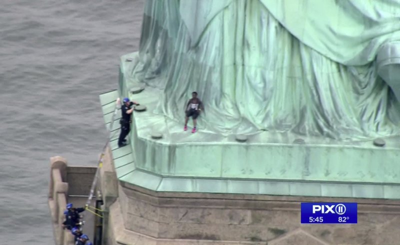 In this image made from video by PIX11, Patricia Okoumou leans against the robes of the Statue of Liberty on Liberty Island, in New York, July 4, 2018. 


