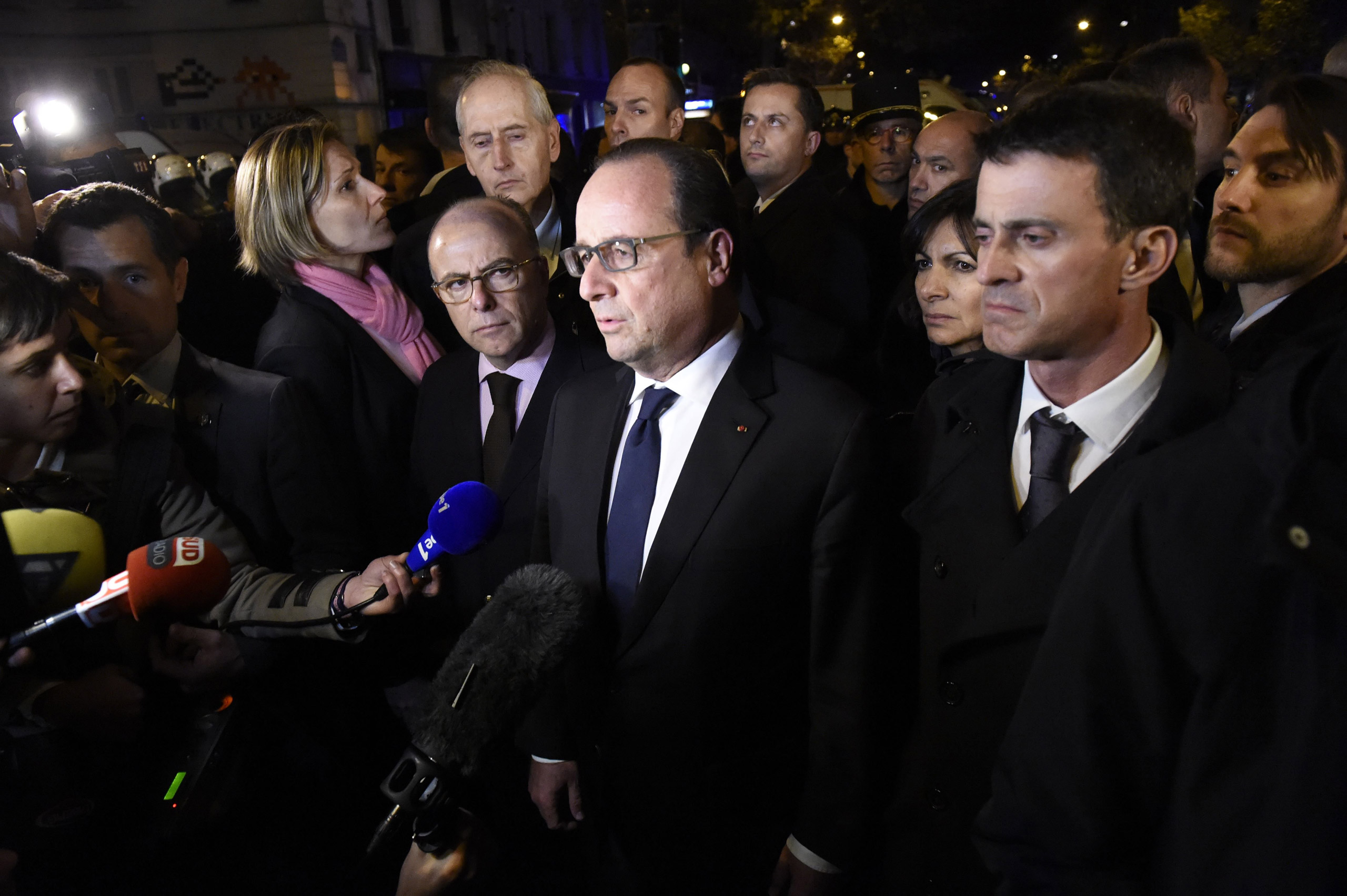 French President Francois Hollande (C), flanked by French Interior Minister Bernard Cazeneuve (L) and French Prime Minister manuel Valls (R) addresses reporters near the Bataclan concert hall in central Paris, early on November 14, 2015. A number of peop