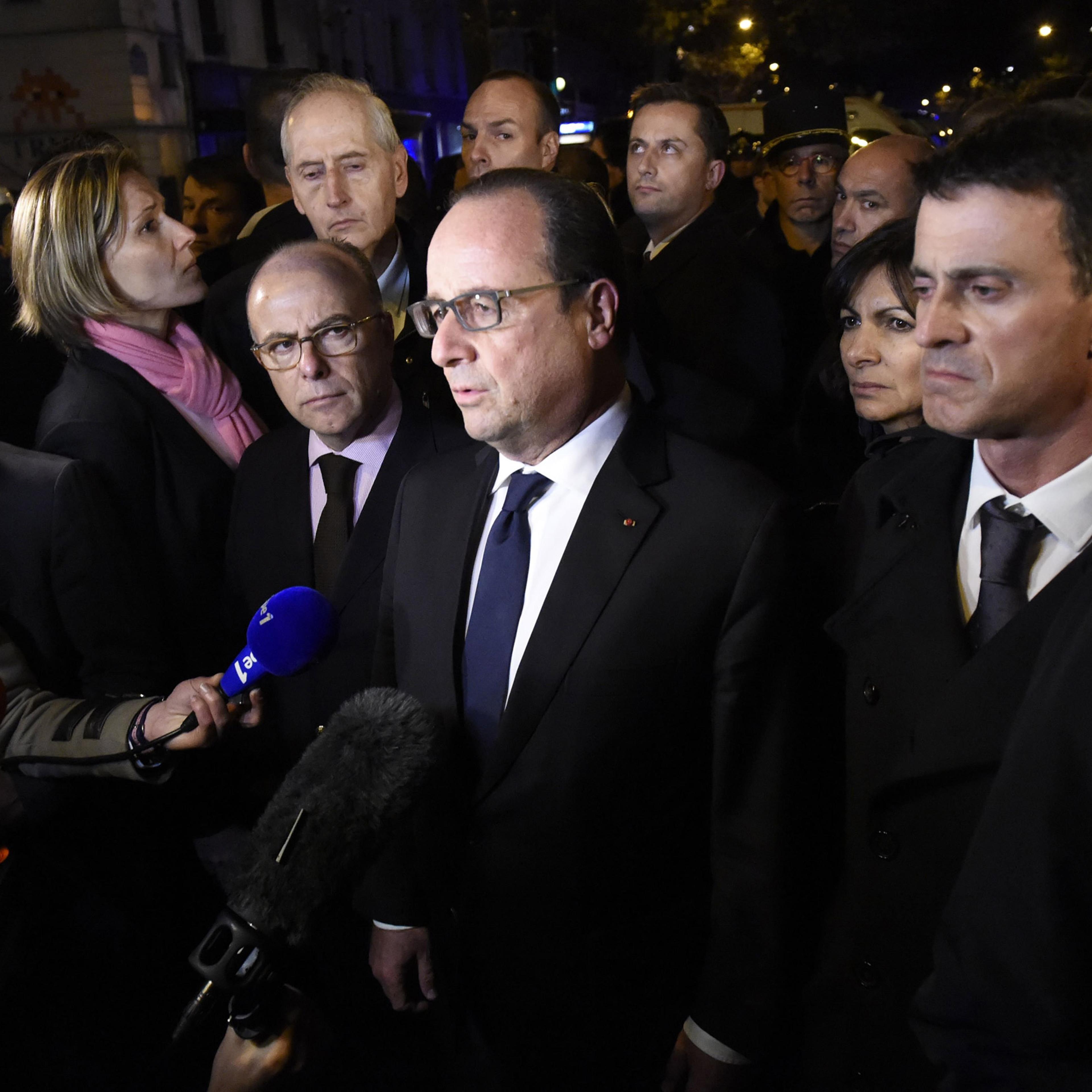 French President Francois Hollande (C), flanked by French Interior Minister Bernard Cazeneuve (L) and French Prime Minister manuel Valls (R) addresses reporters near the Bataclan concert hall in central Paris, early on November 14, 2015. A number of peop