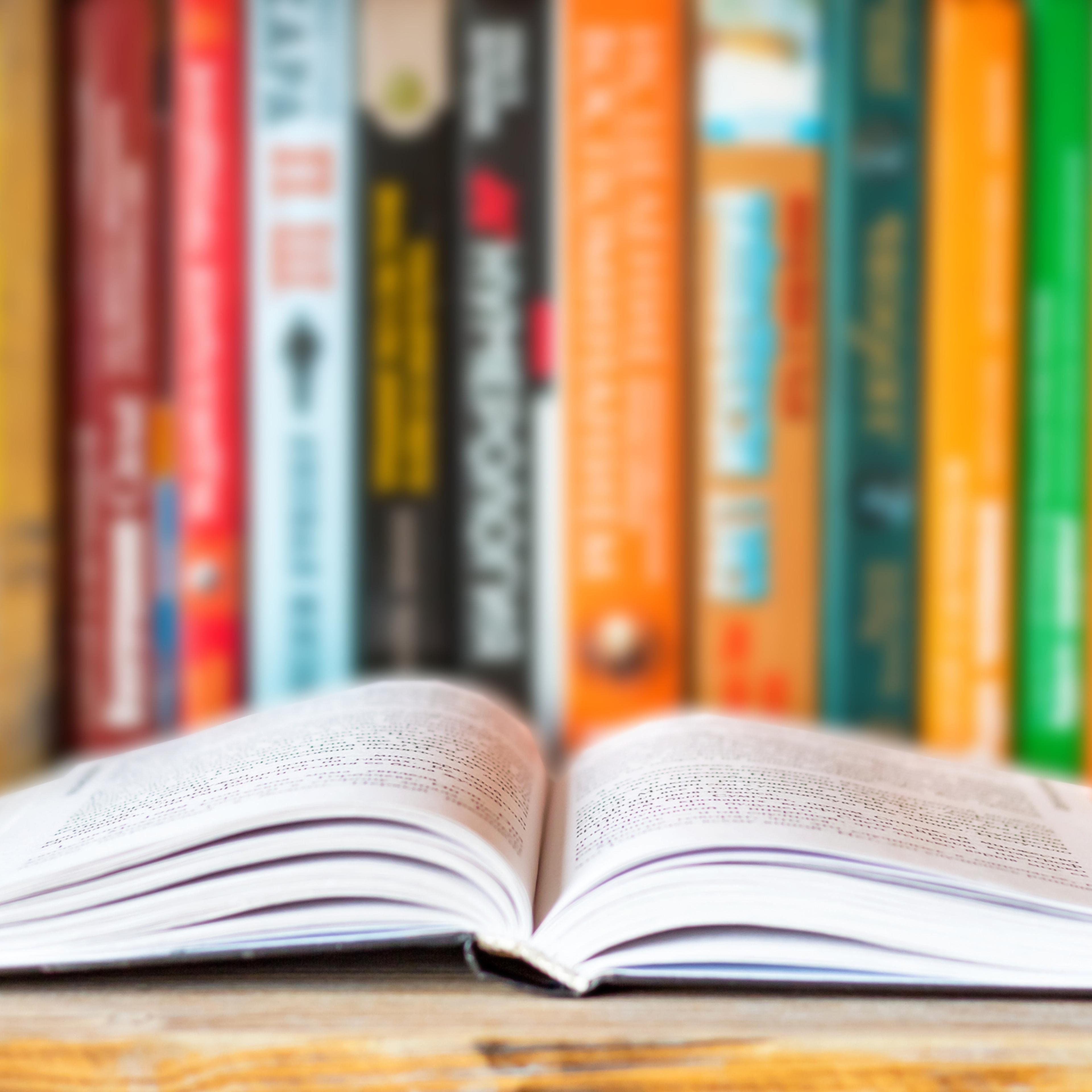 Close-up of opened book on bookshelf on blurred books background. Home library reading books concept
