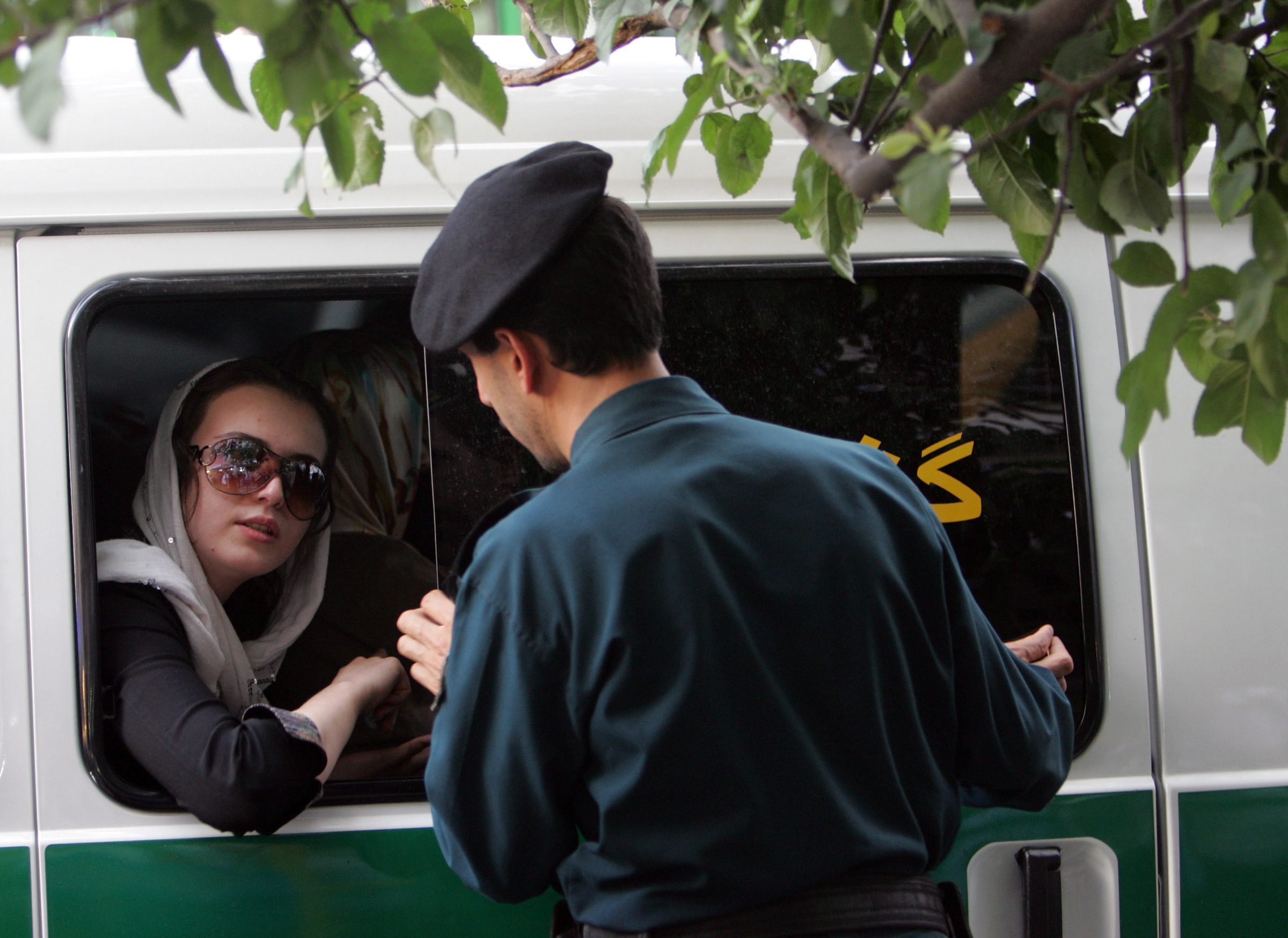 An Iranian policeman (R) speaks with a woman siting in a police car after she was arrested because of her "inappropriate" clothes during a crackdown to enforce Islamic dress code in Tehran, 23 July 2007. 