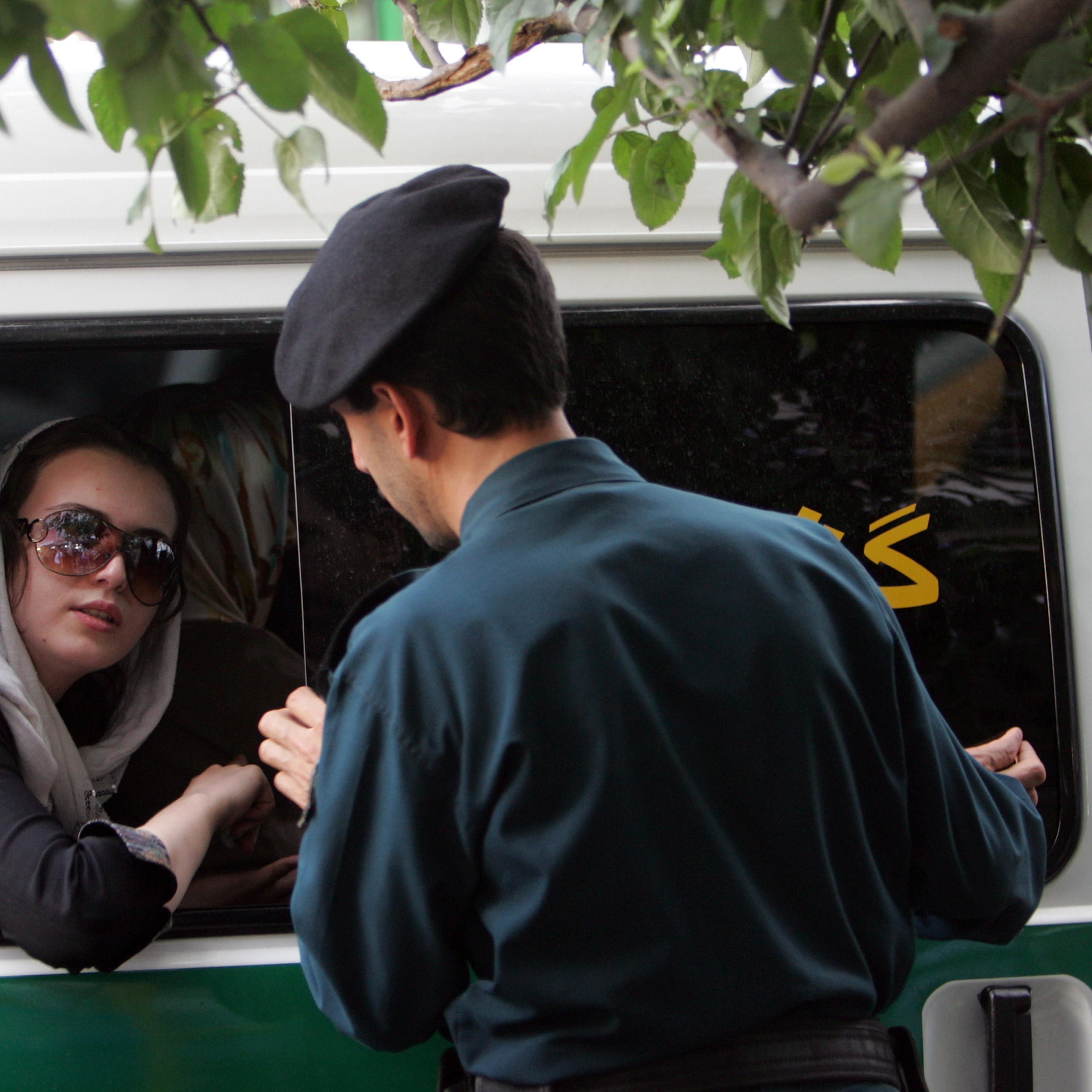 An Iranian policeman (R) speaks with a woman siting in a police car after she was arrested because of her "inappropriate" clothes during a crackdown to enforce Islamic dress code in Tehran, 23 July 2007.