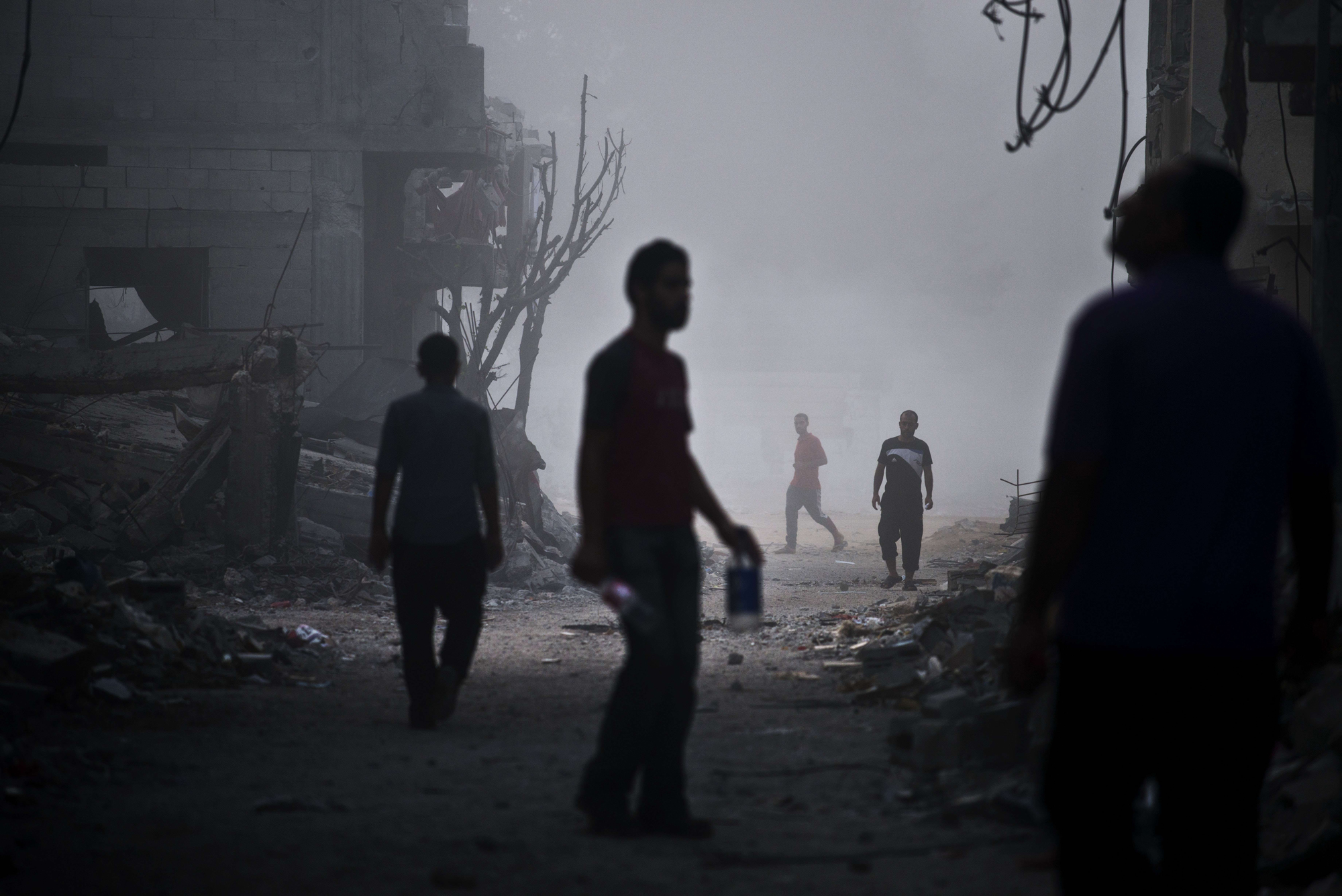 Palestinian men walk in a street of Gaza City's Shejaiya neighborhood in early morning dense fog among the ruins of their neighbourhood on Aug. 27, 2014.