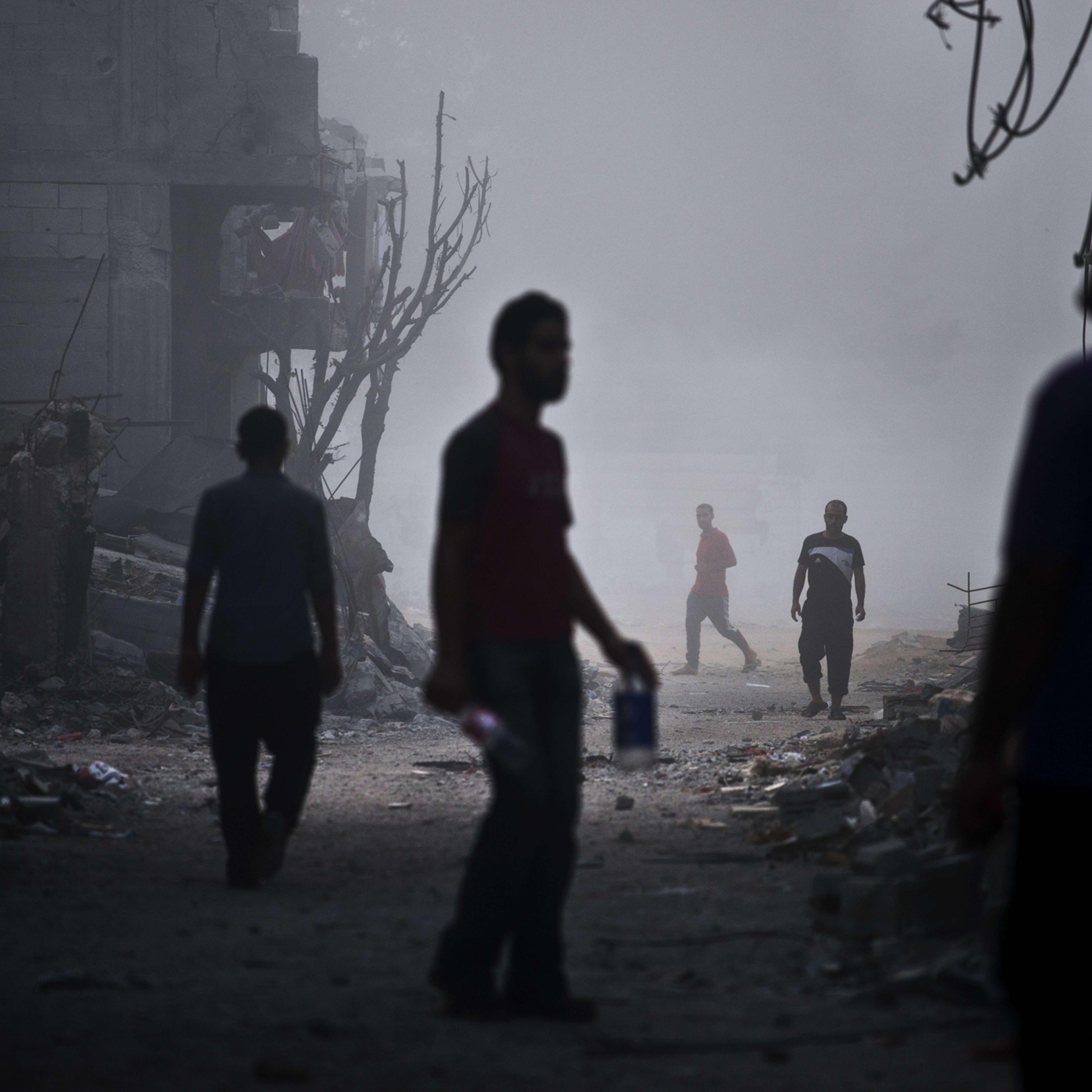 Palestinian men walk in a street of Gaza City's Shejaiya neighborhood in early morning dense fog among the ruins of their neighbourhood on Aug. 27, 2014.