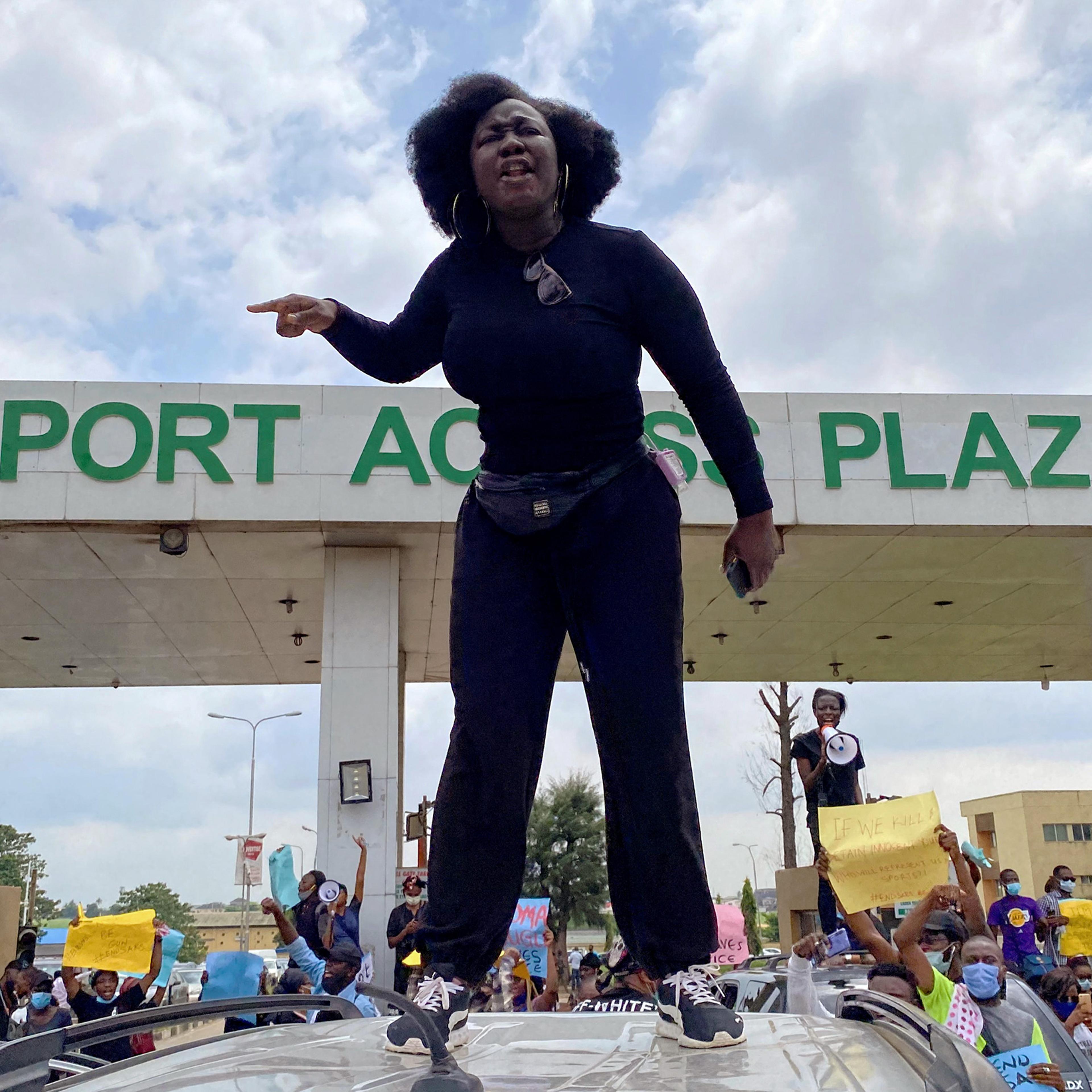 A demonstrator stands atop a vehicle and shouts slogans as others carry banners while blocking a road leading to the airport in Lagos on Oct. 12, 2020.