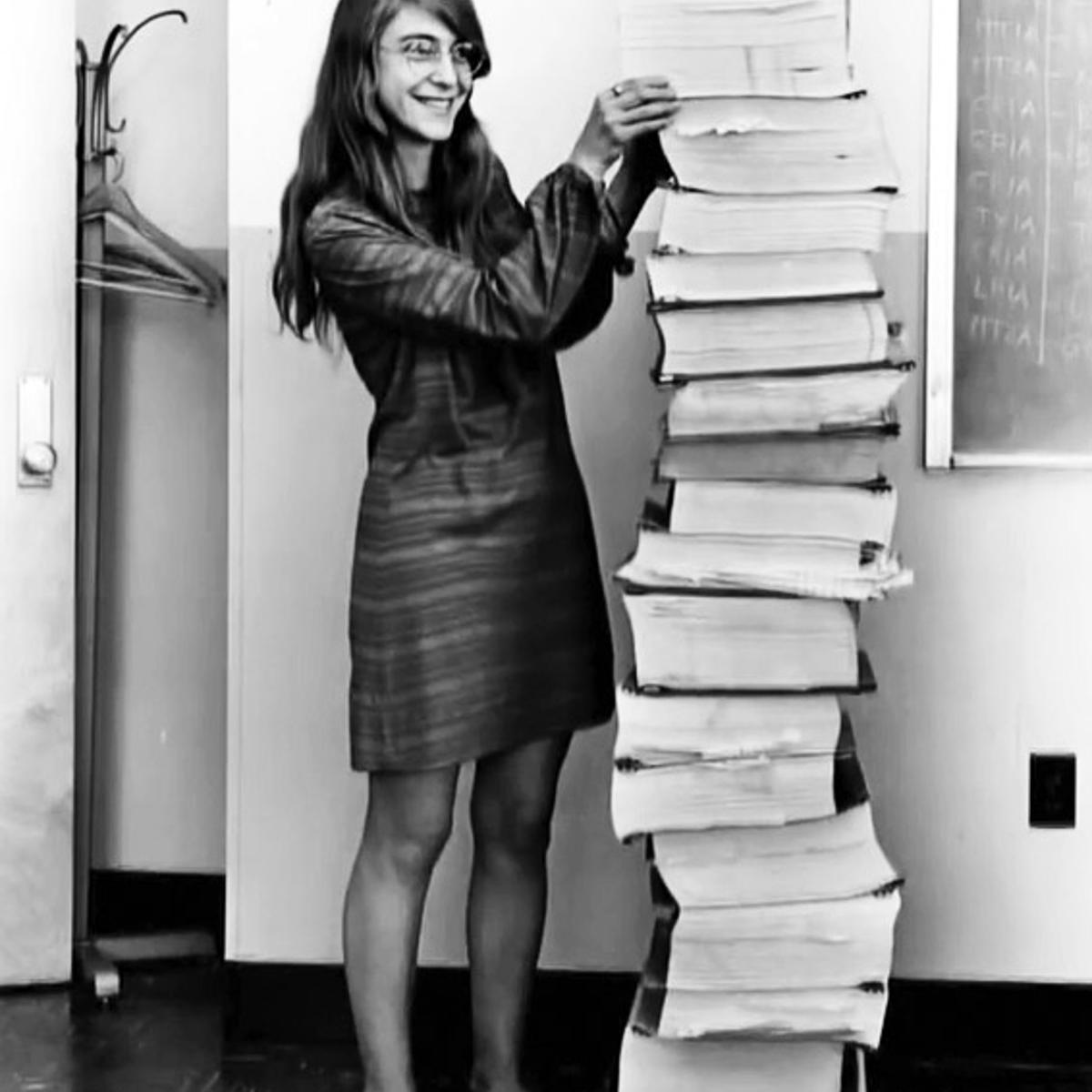 Margaret Hamilton standing next to listings of the actual Apollo Guidance Computer (AGC) source code.