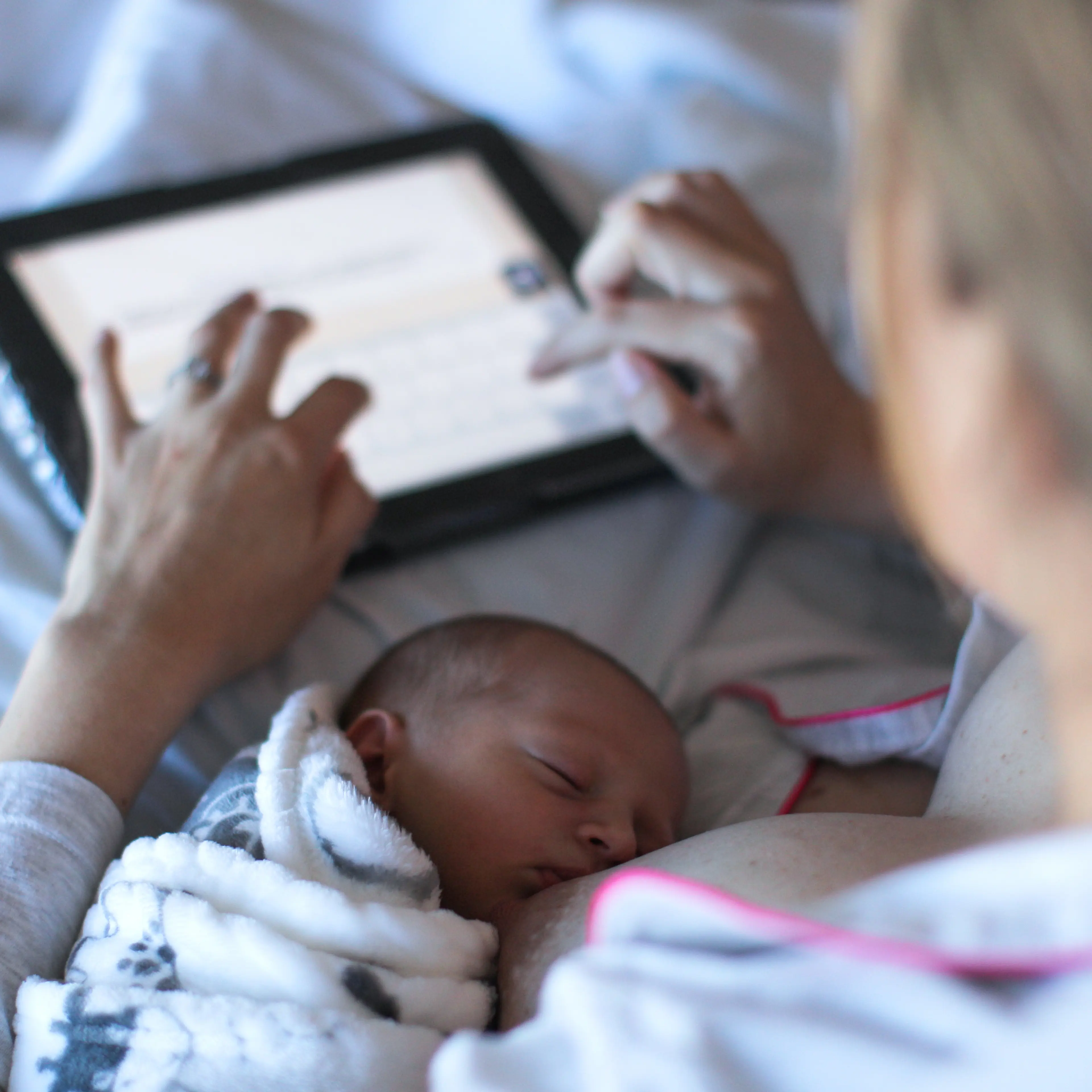 a Young woman fills in a revue of the hospital she gave birth in on a digital tablet while breastfeeding.
