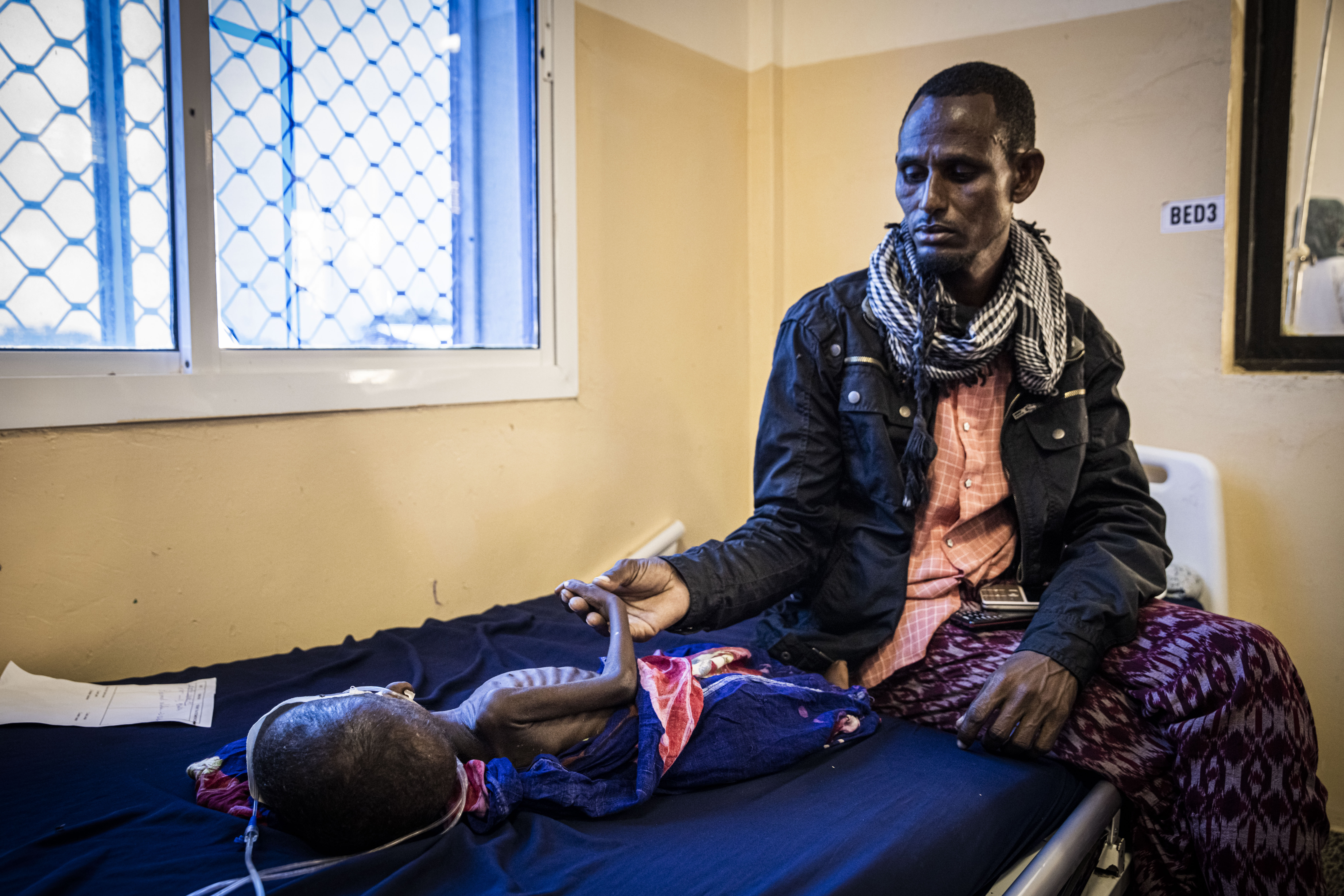 A man holds the hand of his baby who is being treated for severe acute malnutrition at the Banadir Maternity and Children Hospital in Mogadishu, Somalia, on September 4, 2022.