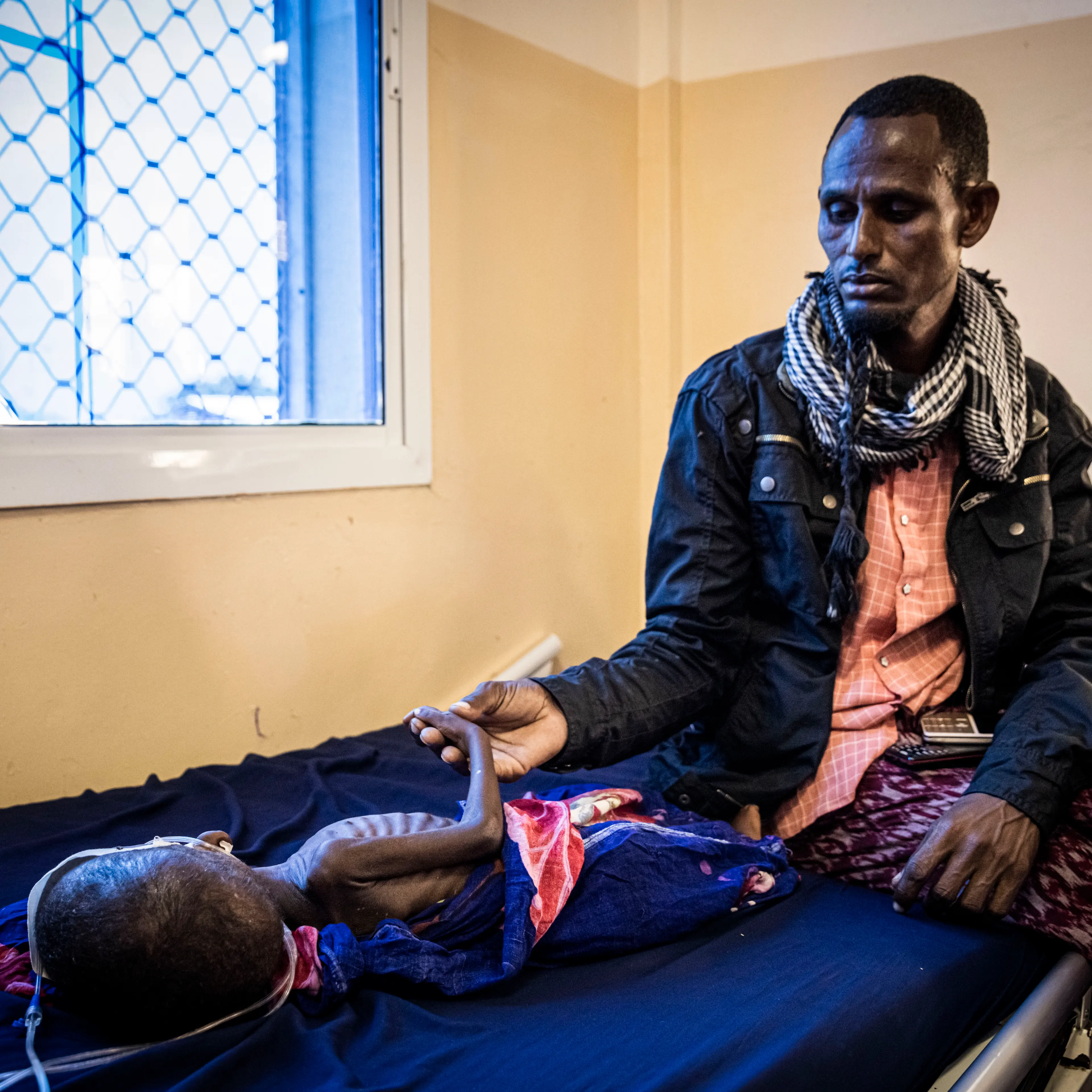 A man holds the hand of his baby who is being treated for severe acute malnutrition at the Banadir Maternity and Children Hospital in Mogadishu, Somalia, on September 4, 2022.