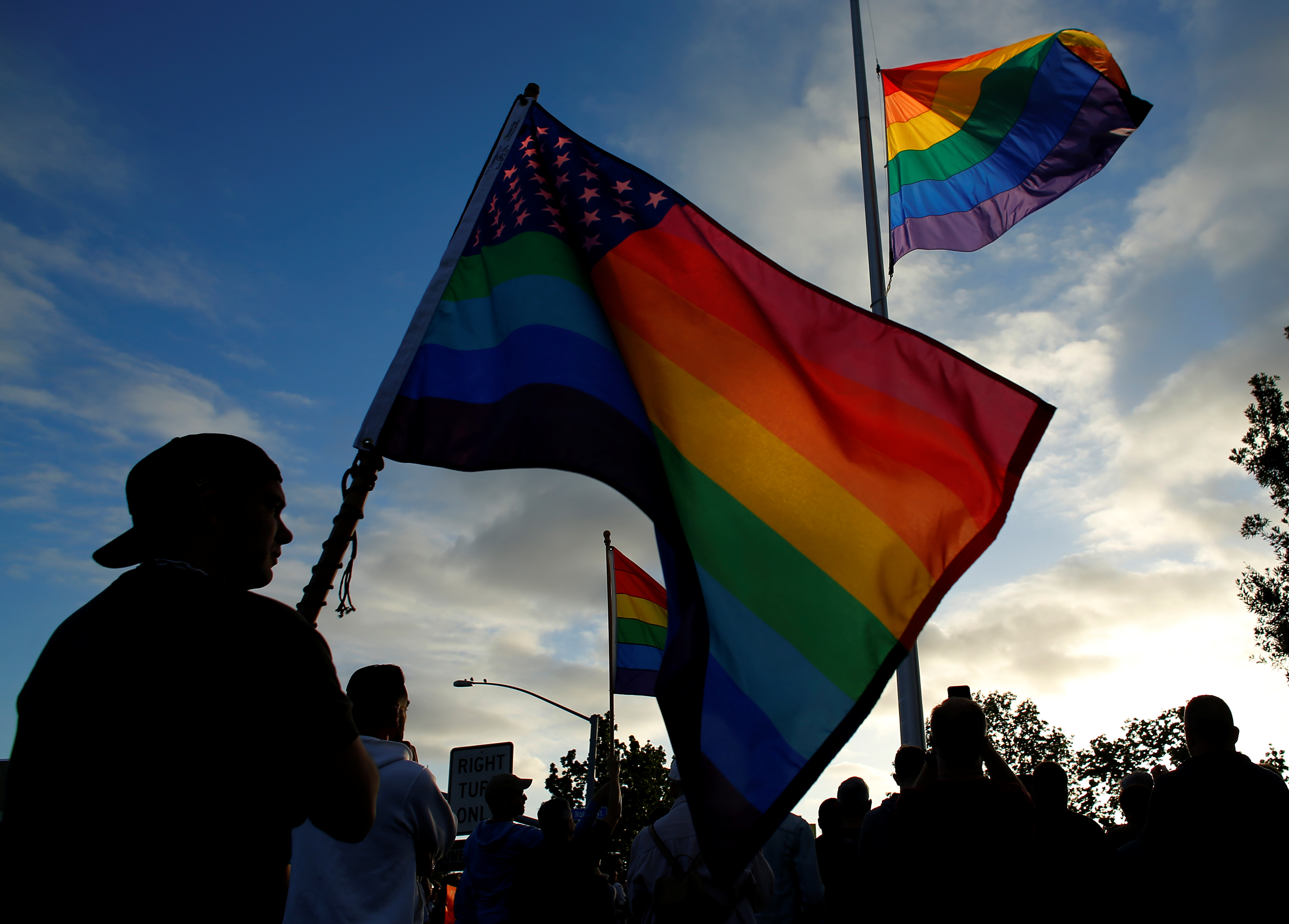 Mourners gather under an LGBT pride flag flying at half-mast for a candlelight vigil in remembrance for mass shooting victims in Orlando, from San Diego, California