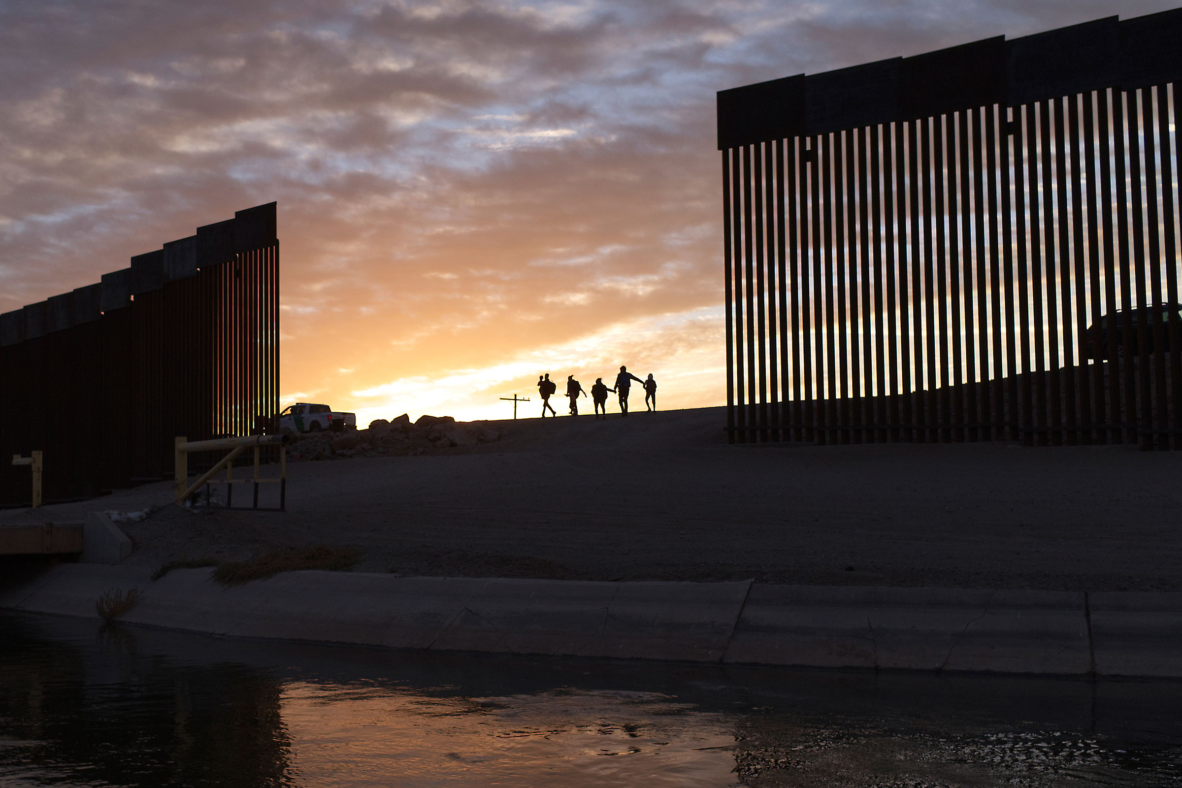 A pair of migrant families from Brazil pass through a gap in the border wall