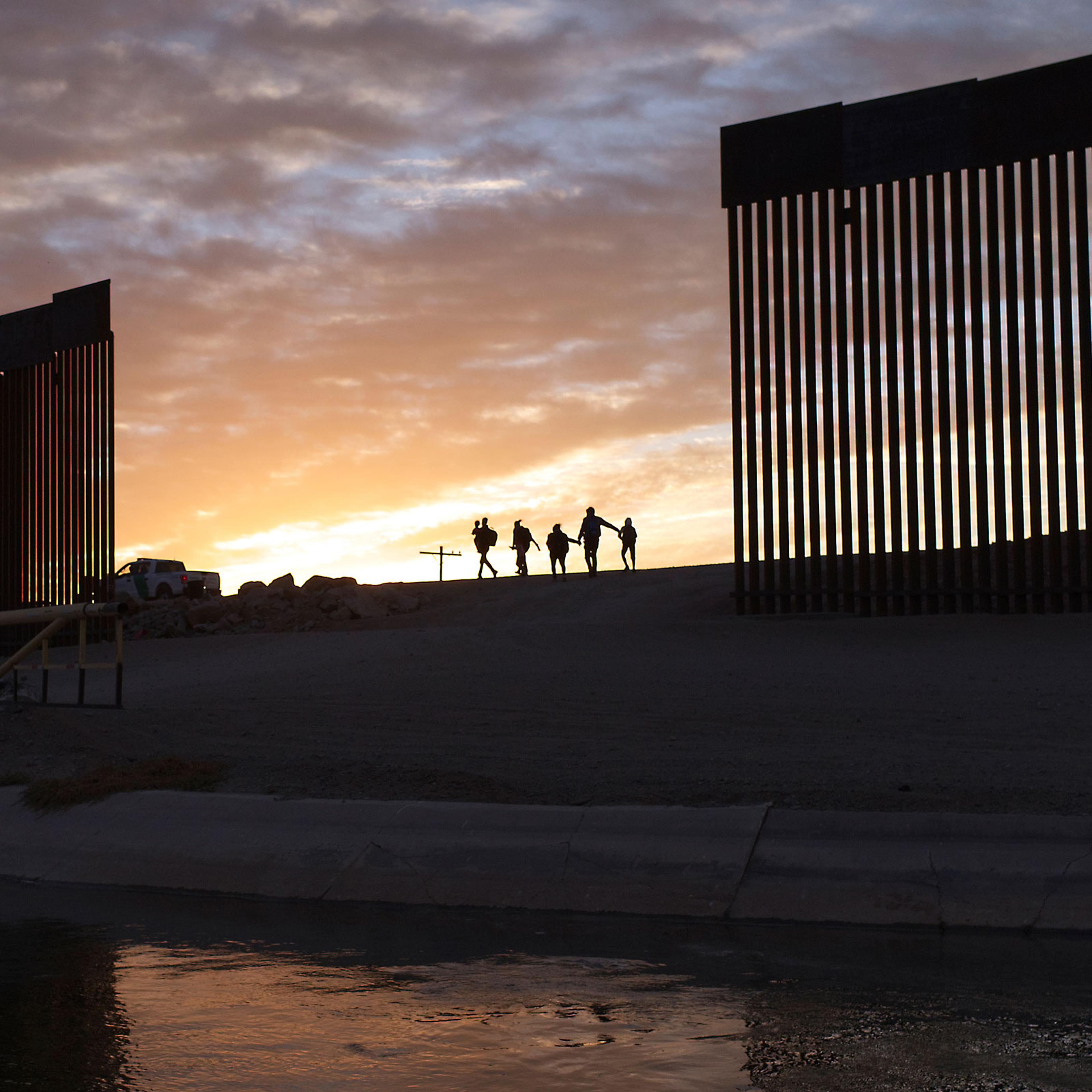 A pair of migrant families from Brazil pass through a gap in the border wall