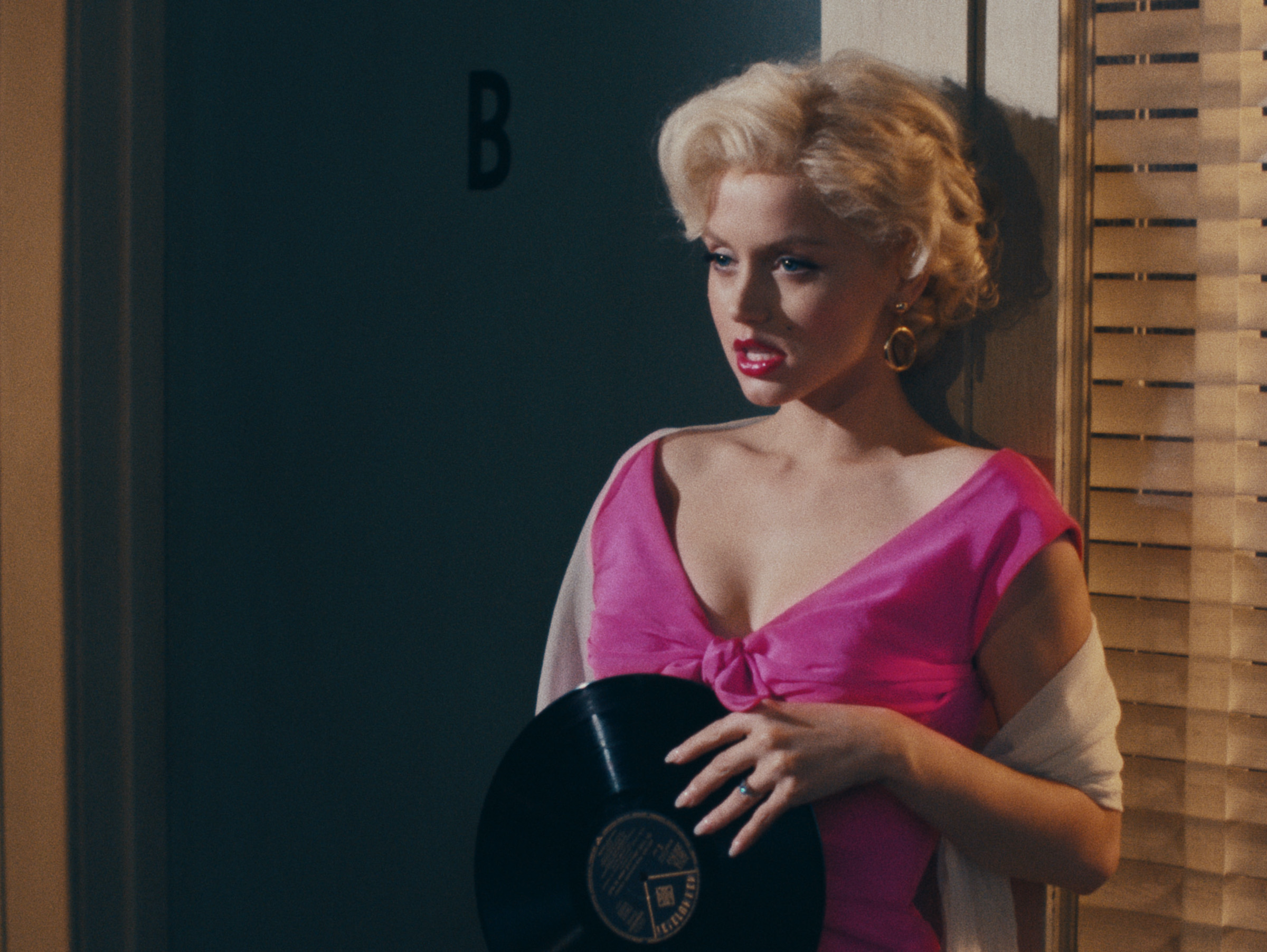Ana de Armas as Marilyn Monroe clutches a record to her chest in a bright pink dress.