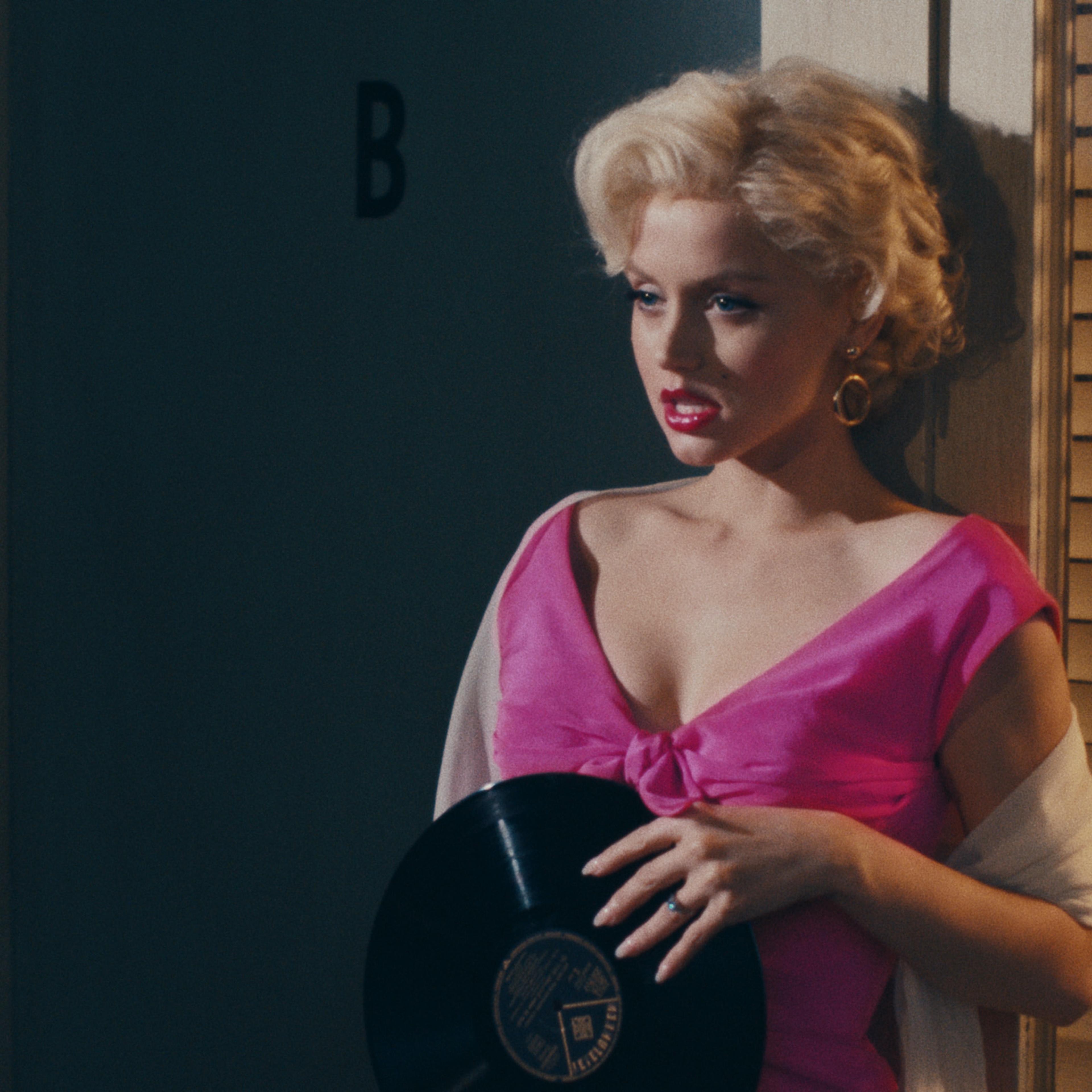 Ana de Armas as Marilyn Monroe clutches a record to her chest in a bright pink dress.