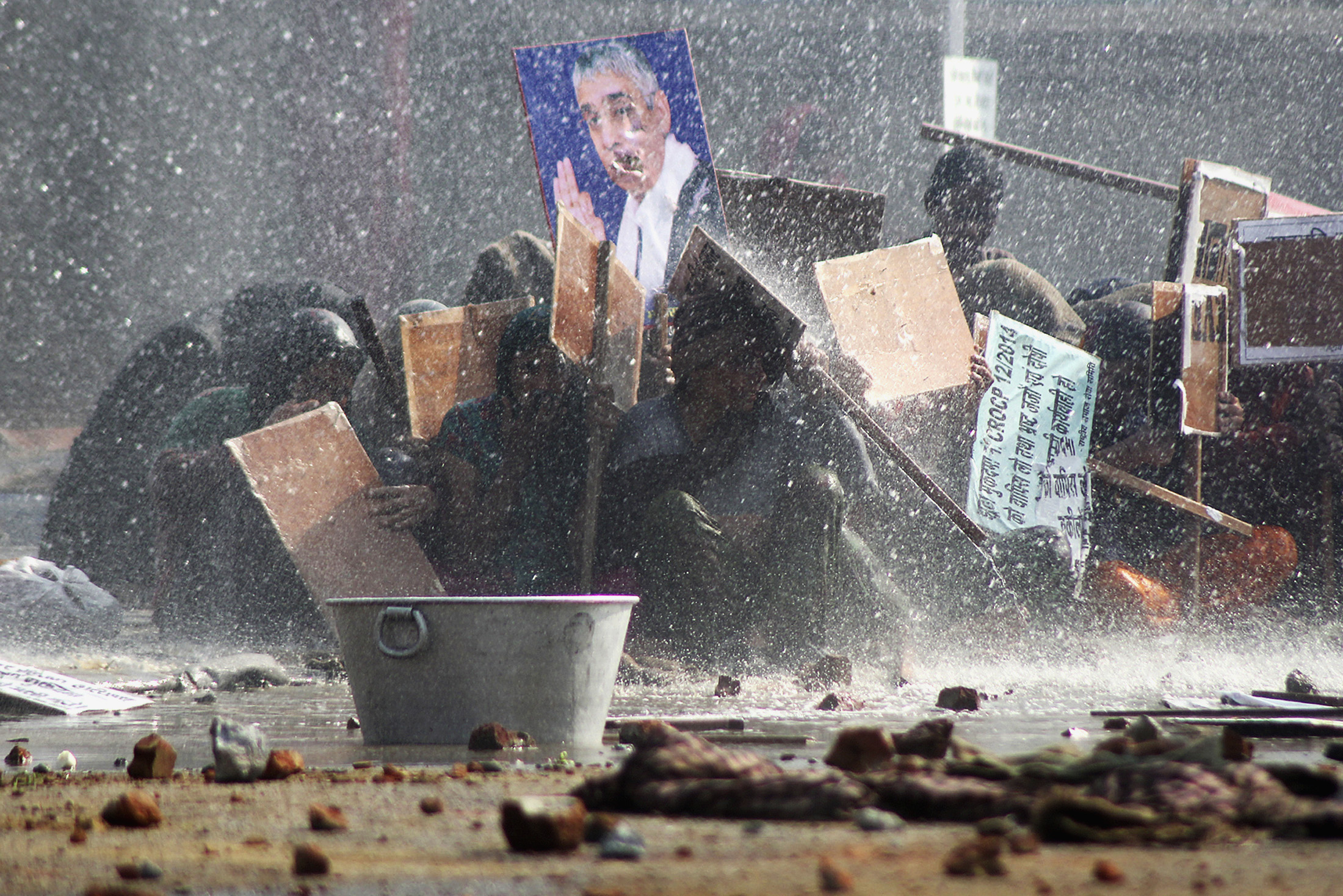 Supporters of Satguru Rampalji Maharaj, a self-styled "godman" take shelter under placards as they are hit by a police water cannon during a protest outside the ashram of Rampal in Hisar