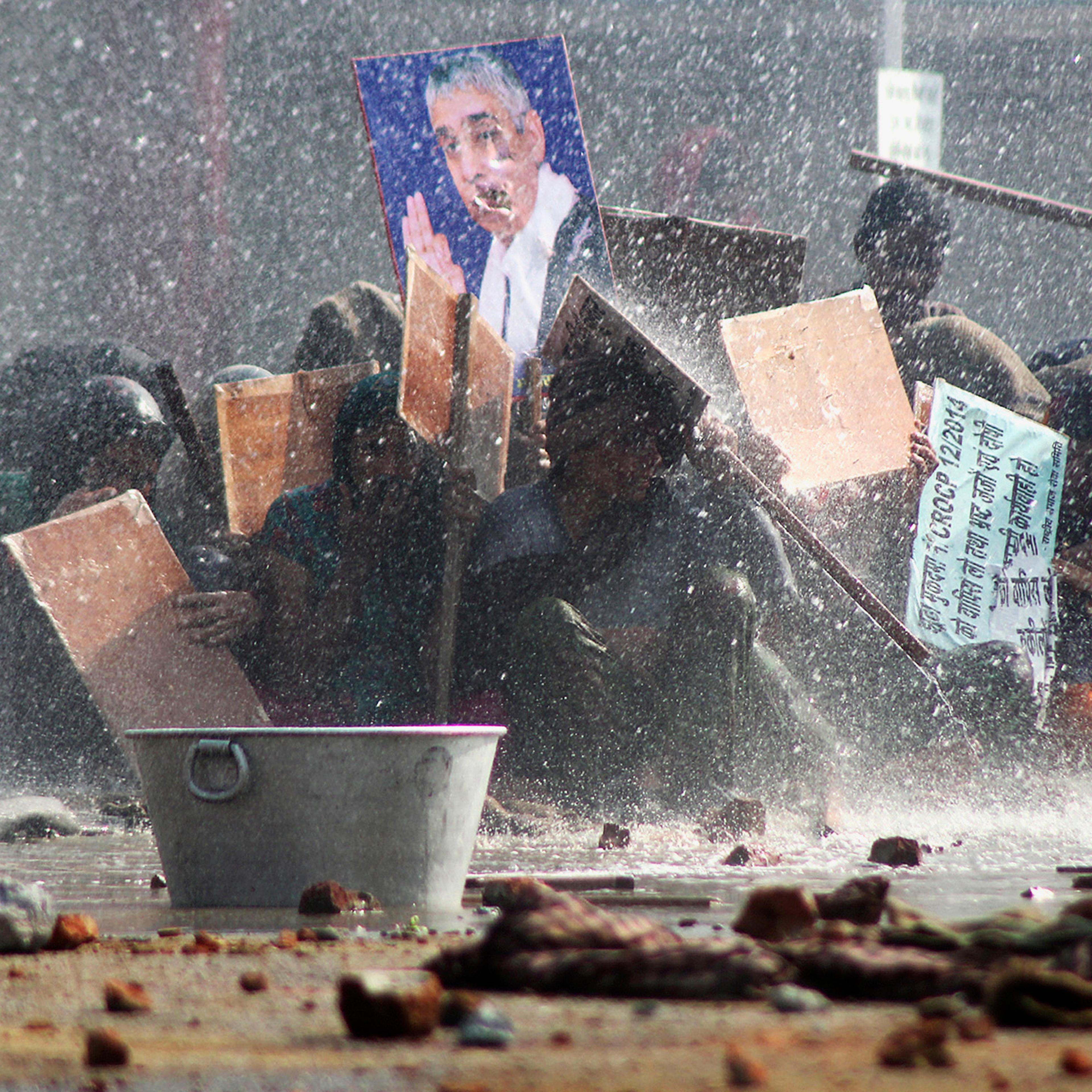 Supporters of Satguru Rampalji Maharaj, a self-styled "godman" take shelter under placards as they are hit by a police water cannon during a protest outside the ashram of Rampal in Hisar