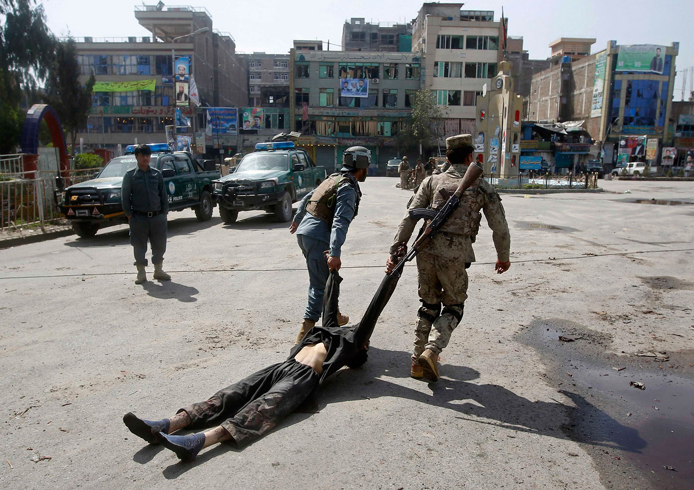 Afghan policemen remove the dead body of a Taliban insurgent from the site of a suicide car bomb attack in Jalalabad province, March 20, 2014.