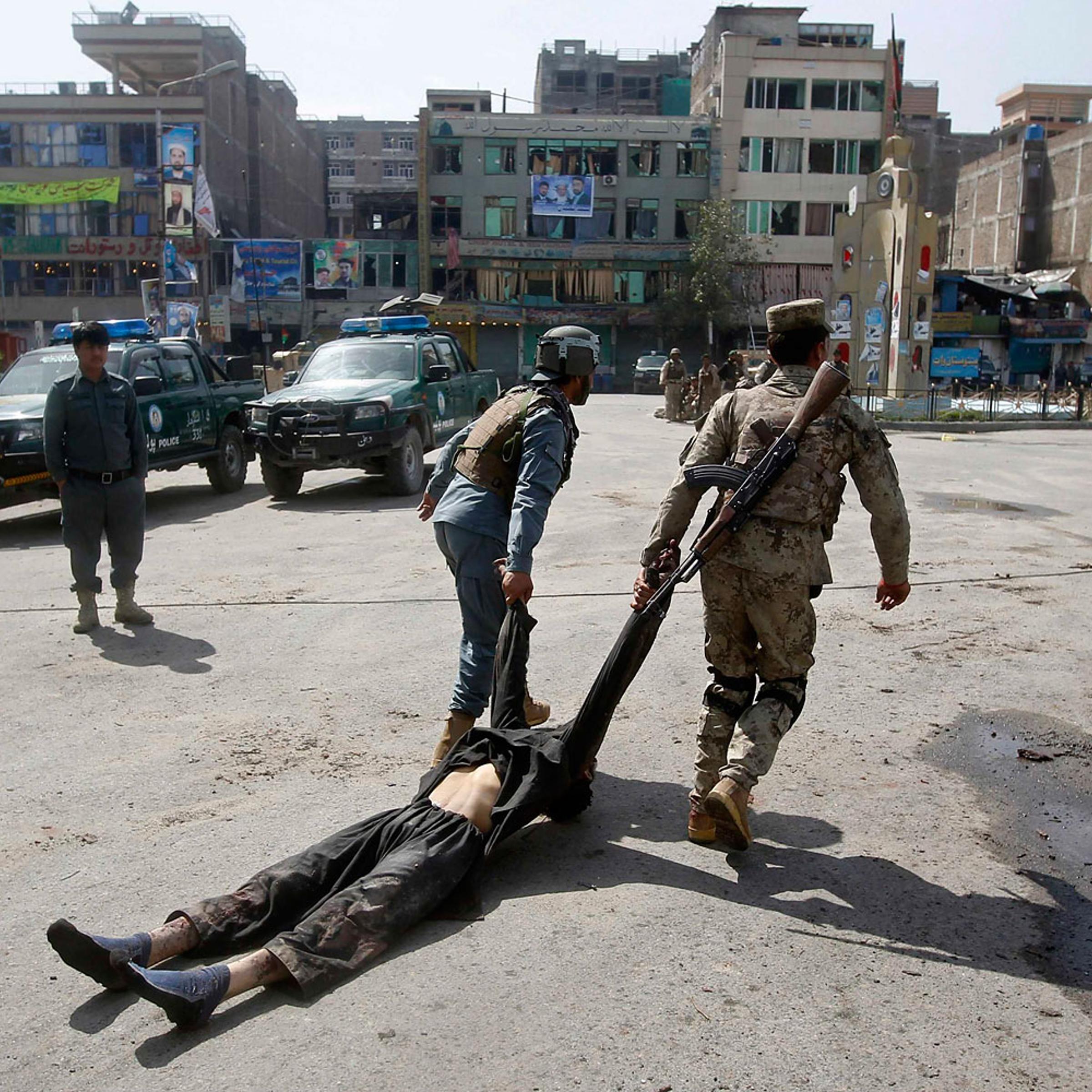 Afghan policemen remove the dead body of a Taliban insurgent from the site of a suicide car bomb attack in Jalalabad province, March 20, 2014.
