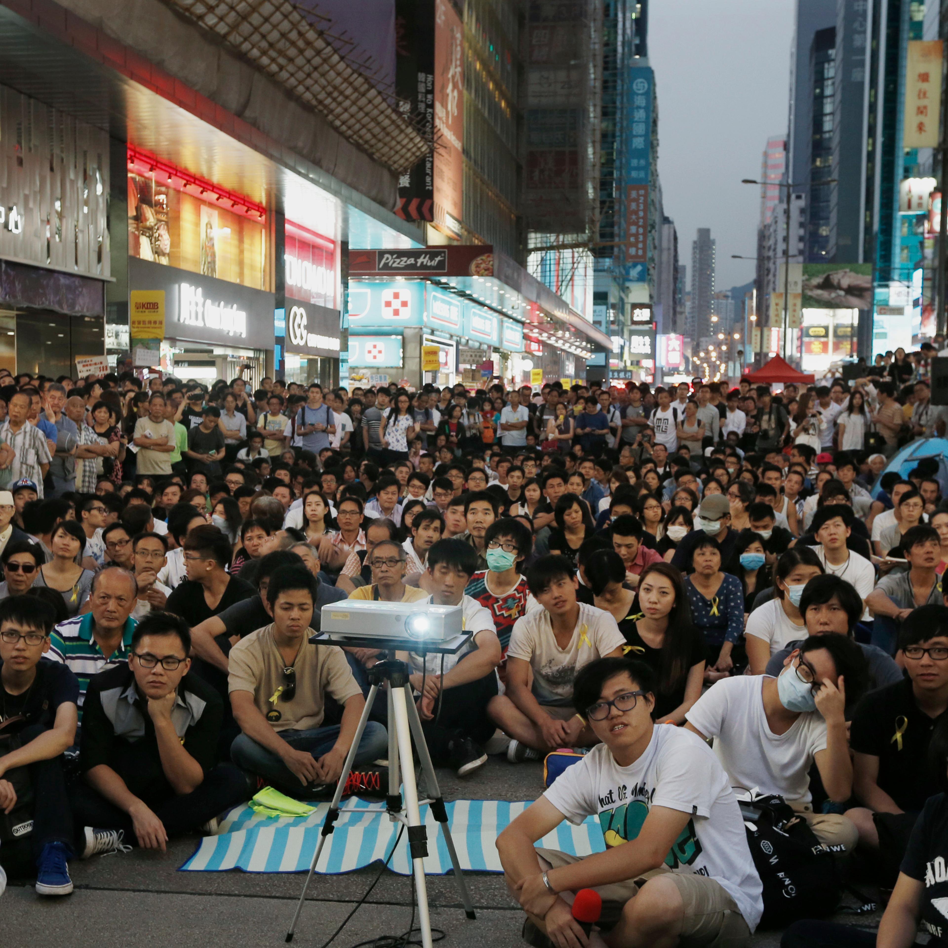 Hundreds of pro-democracy protesters watch a live broadcast of a meeting between student leaders and government officials on a road blocked by them at Mongkok shopping district in Hong Kong