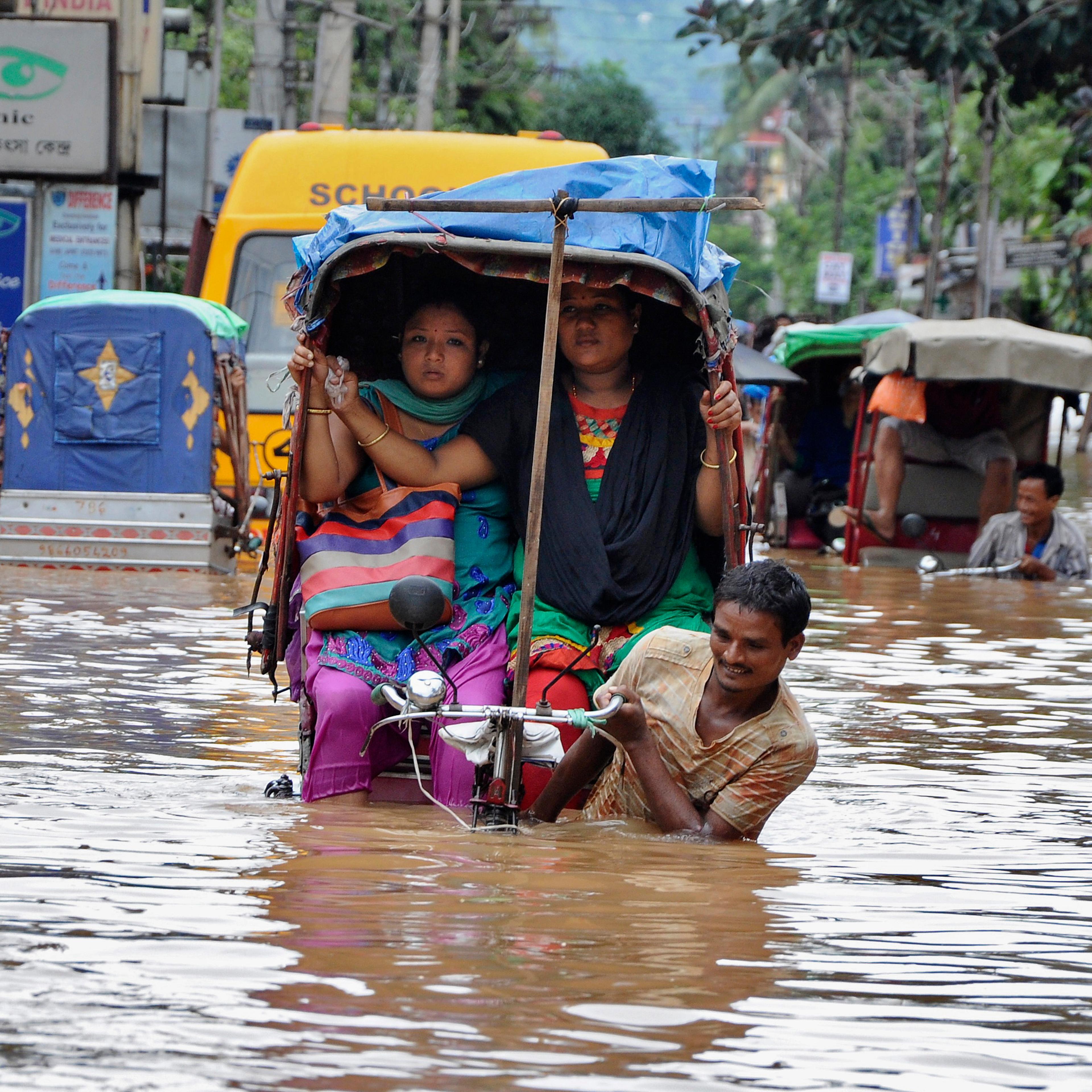 People use cycle rickshaws to commute through a flooded road after heavy rains in Guwahati