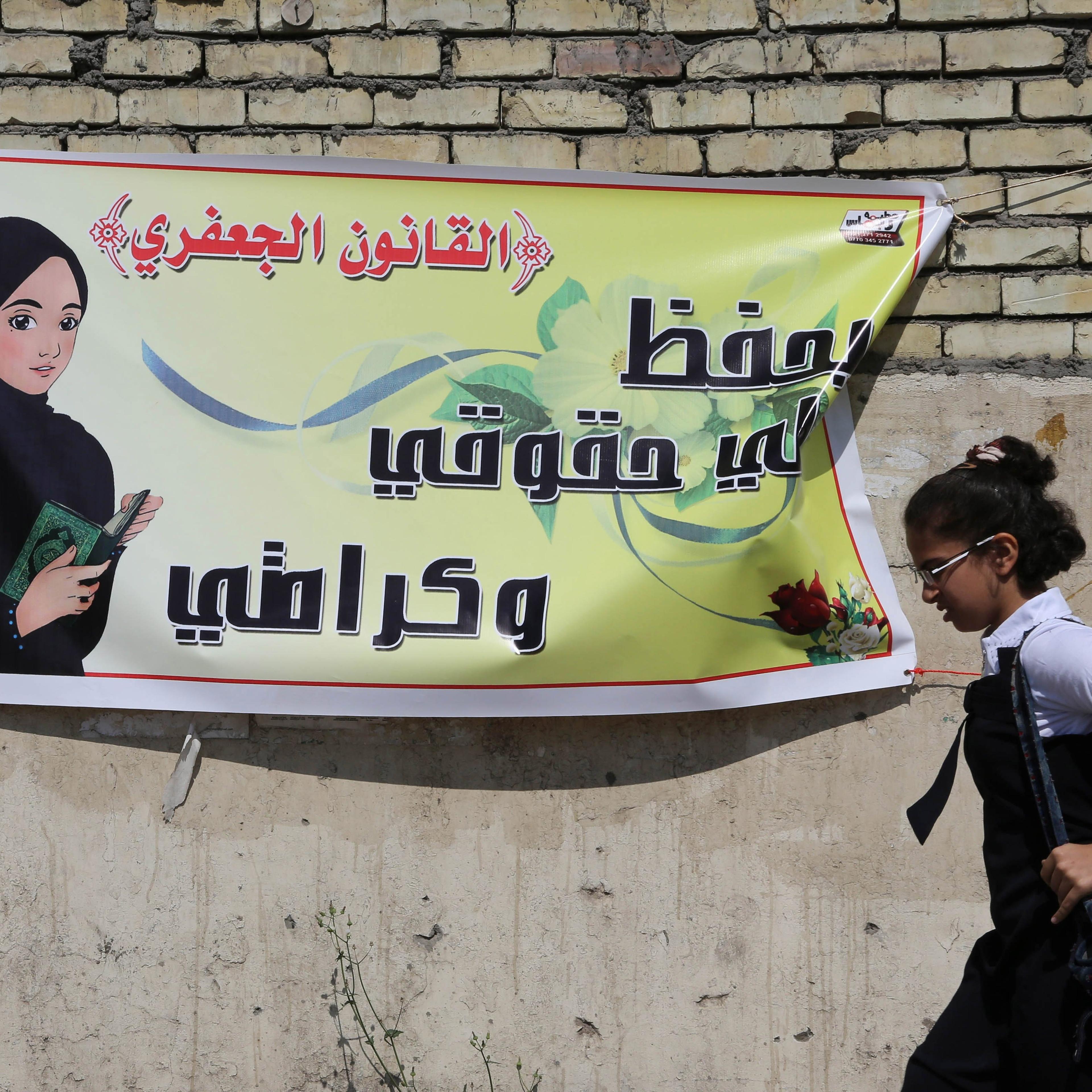 A schoolgirl passes by a banner for the Jaafari Personal Status Law in Baghdad