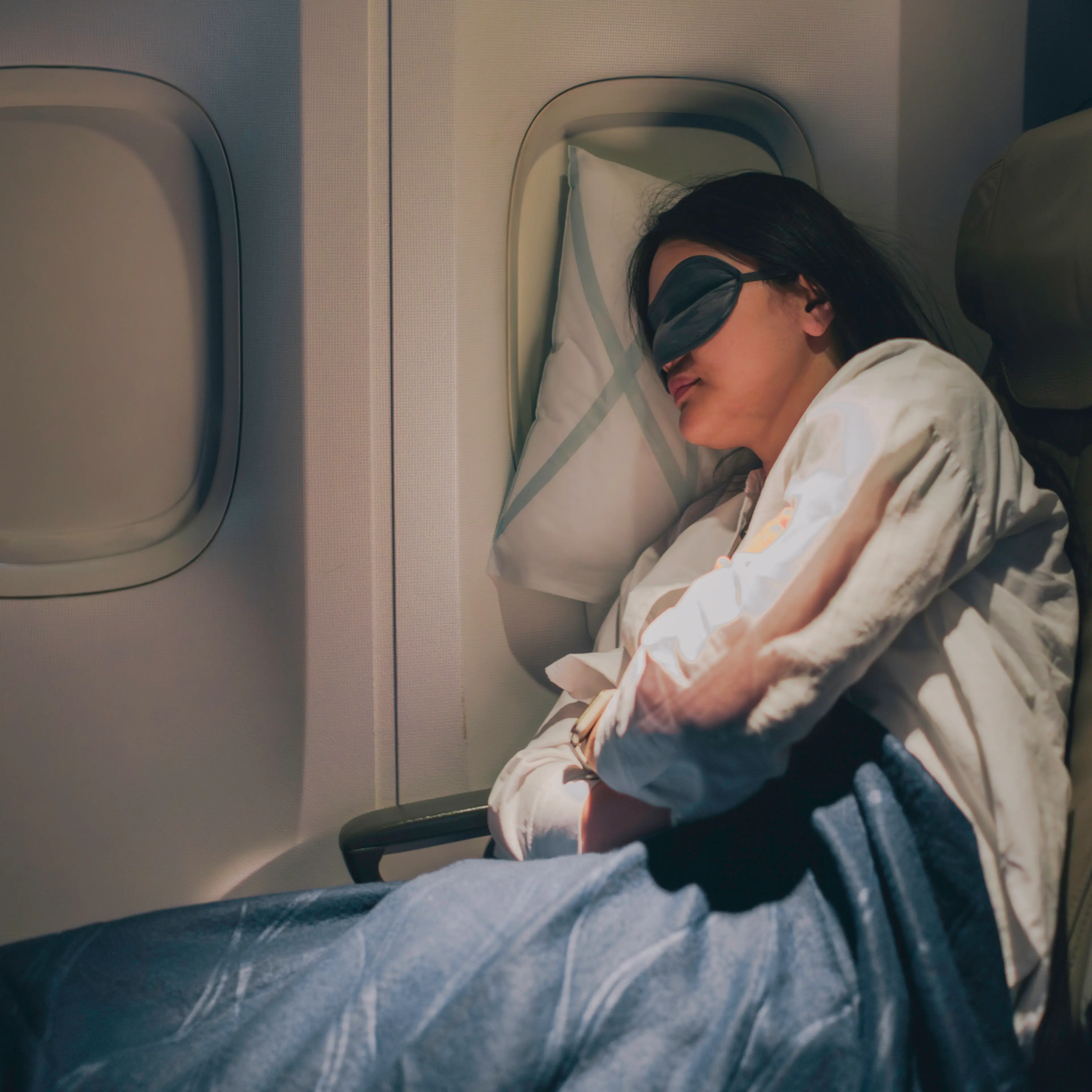 A woman wearing a sleep mask sleeping on a plane