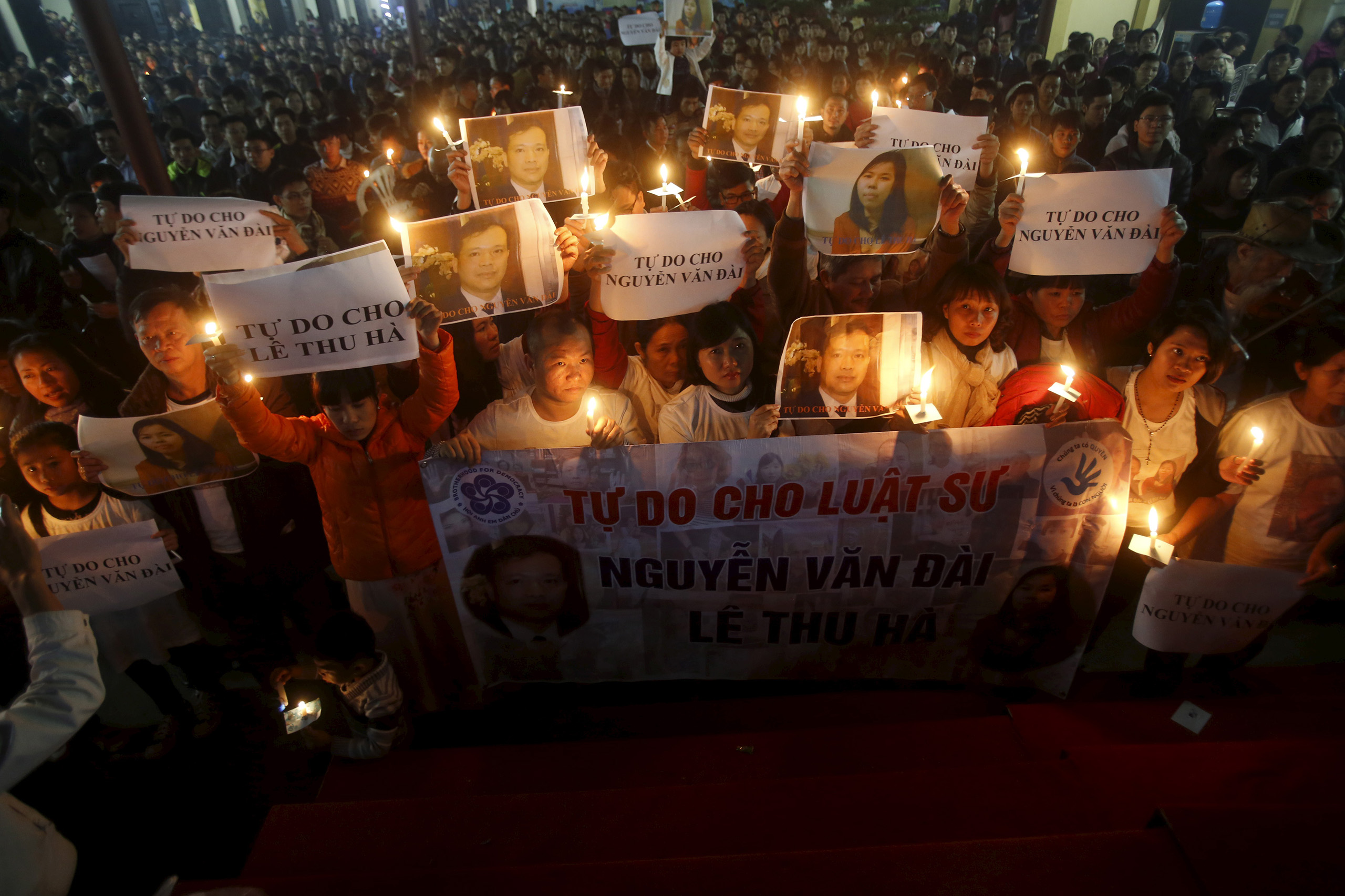 Vu Minh Khanh holds an image of her husband Nguyen Van Dai as Catholics hold candles and image of Dai's assistant Le Thu Ha during a mass prayer for Dai and Ha at Thai Ha church in Hanoi, Dec. 27, 2015.